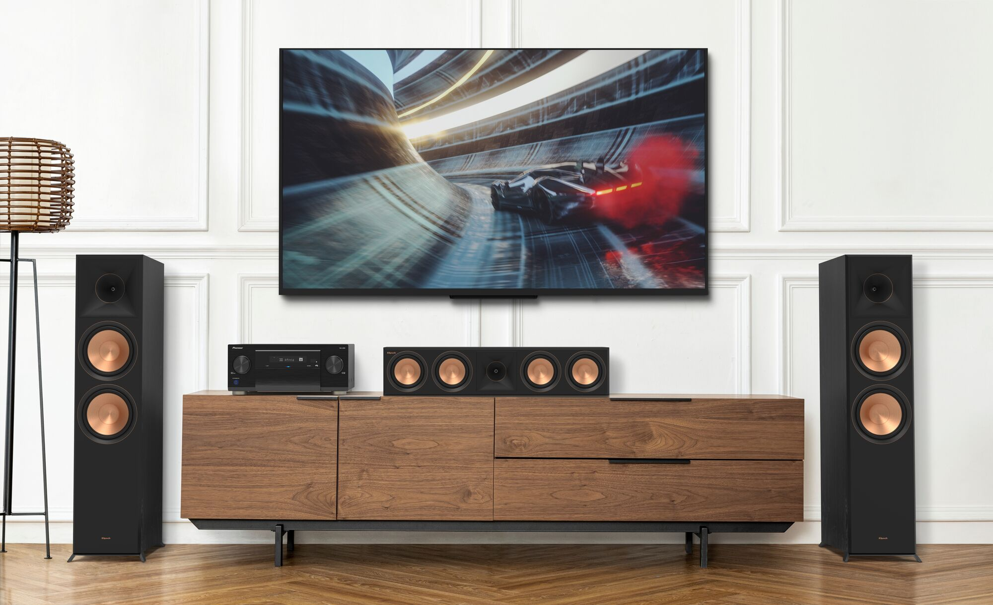 Heimkino-Setup mit großem Fernseher, Lautsprechern und einer Holzkonsolen. Auf dem Fernsehbildschirm ist ein Rennspiel zu sehen.