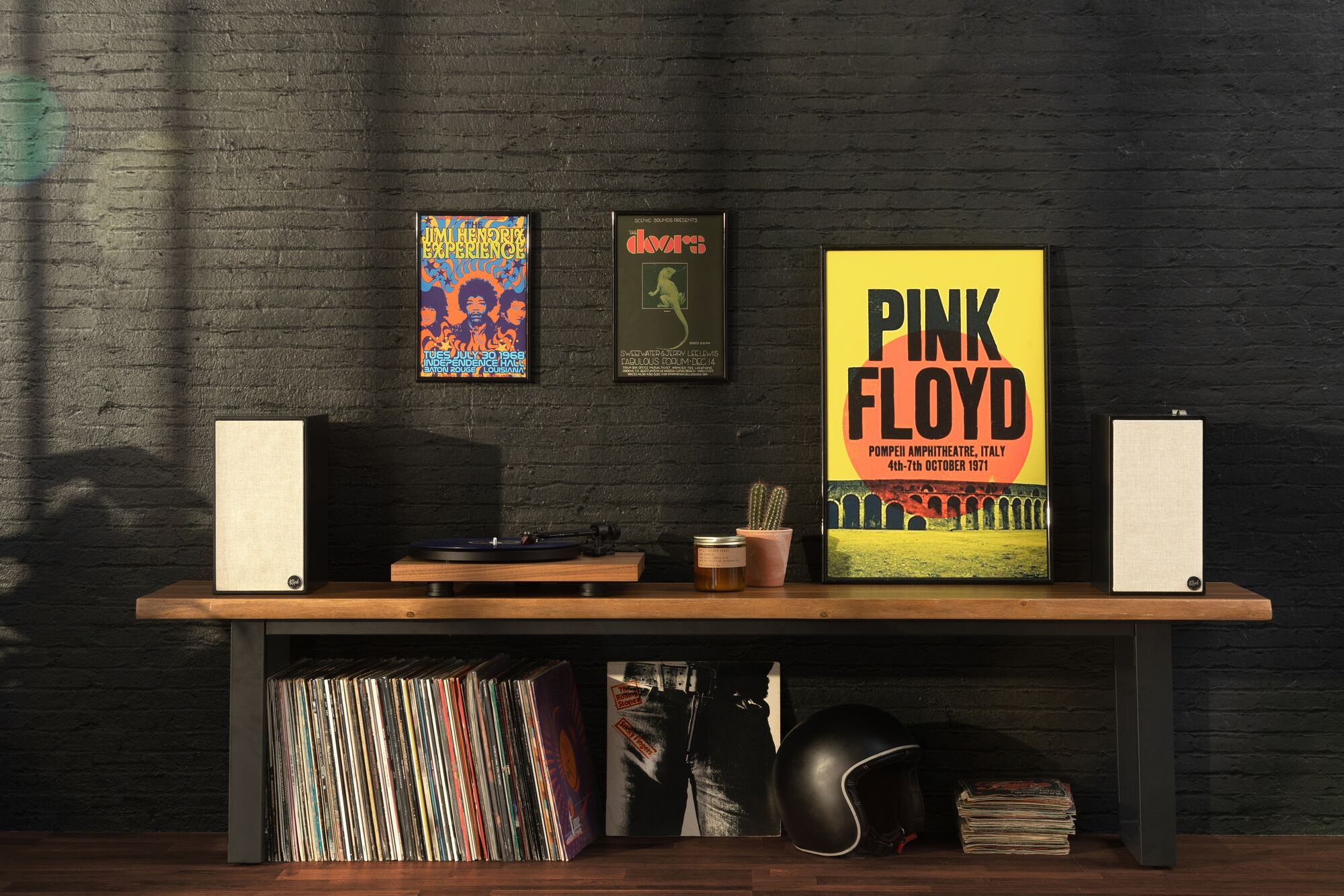 Un ambiente con un giradischi, due altoparlanti, dischi in vinile e poster. Lo sfondo è un muro di mattoni.