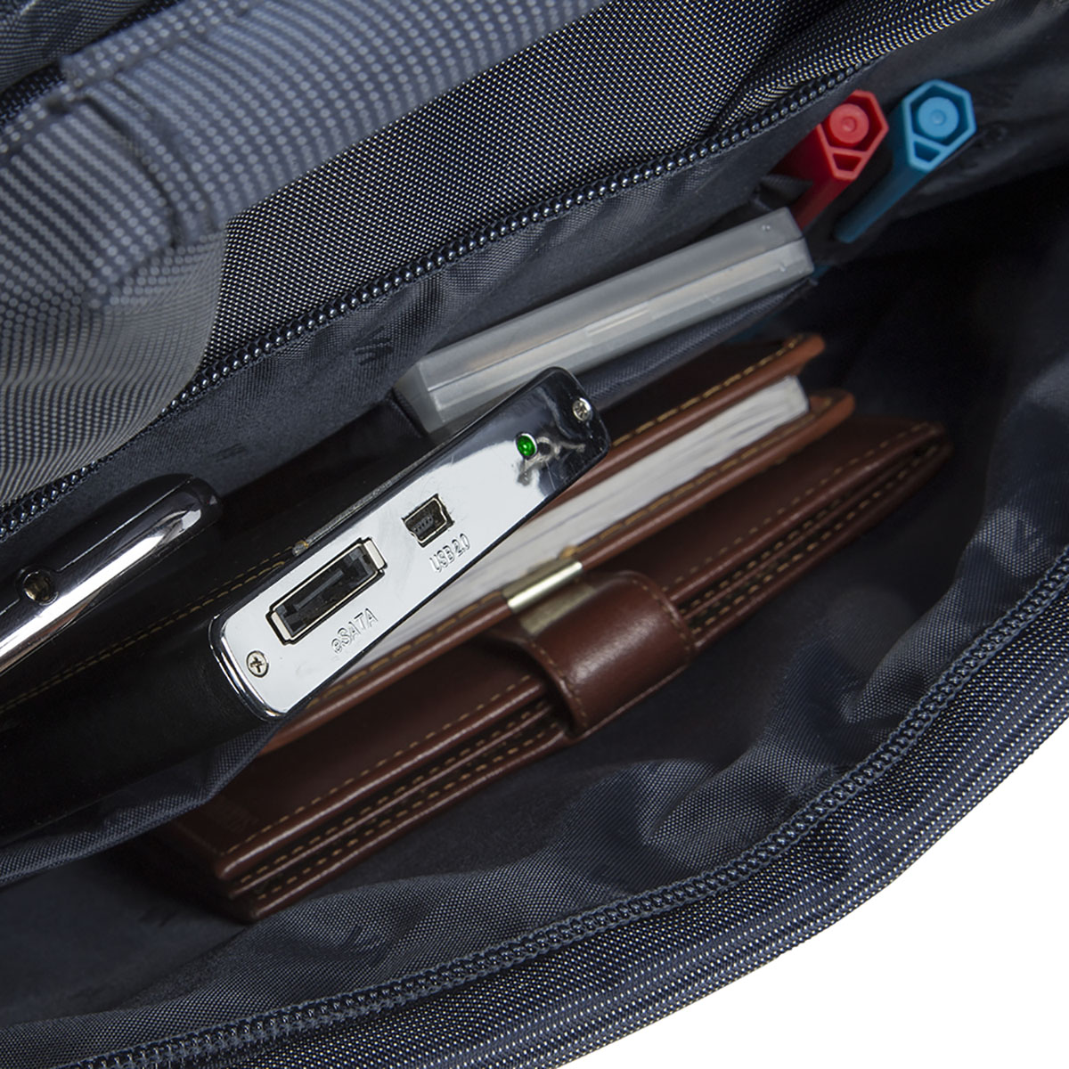 Open bag with pens, a notebook, a USB drive, and a brown leather notebook.