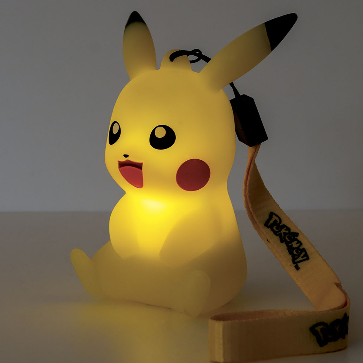 Lámpara Pikachu amarilla brillante con ojos negros, mejillas rojas y correa amarilla, sobre una superficie.