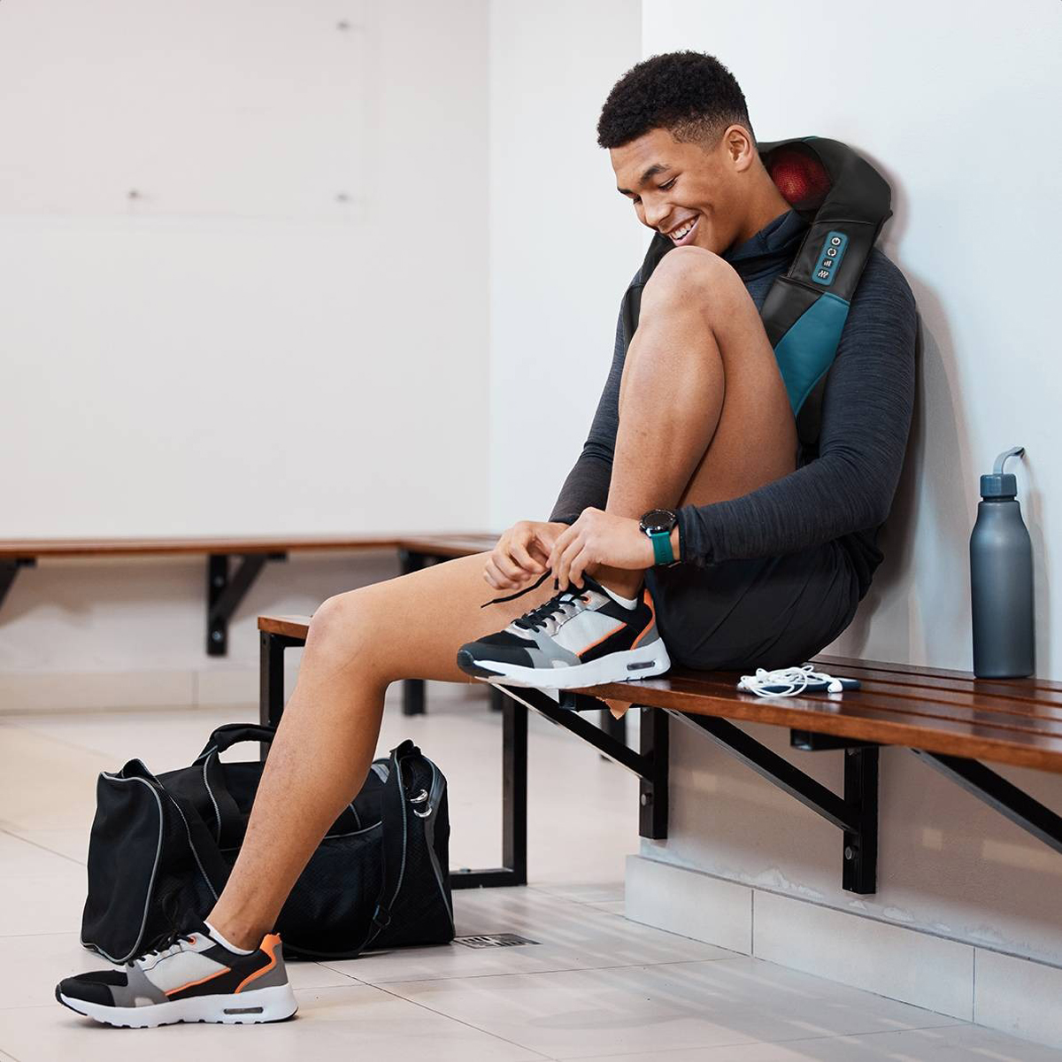 Man wearing a massage neck wrap, sitting on a bench, tying his shoe.