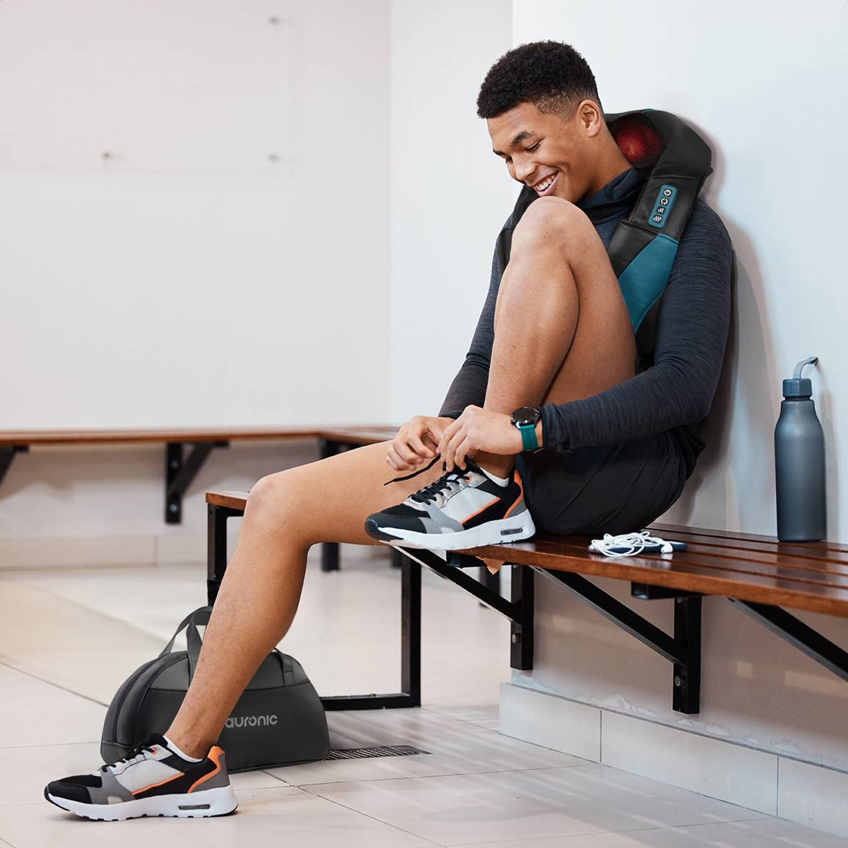 A man laces his shoes. He is wearing a massage device and a watch. A water bottle and a bag are present.