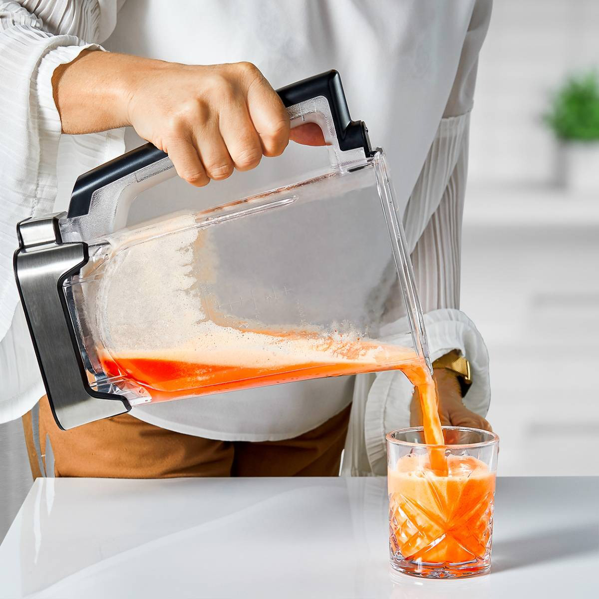 Woman pouring orange juice from a blender into a glass on a white table. White background.
