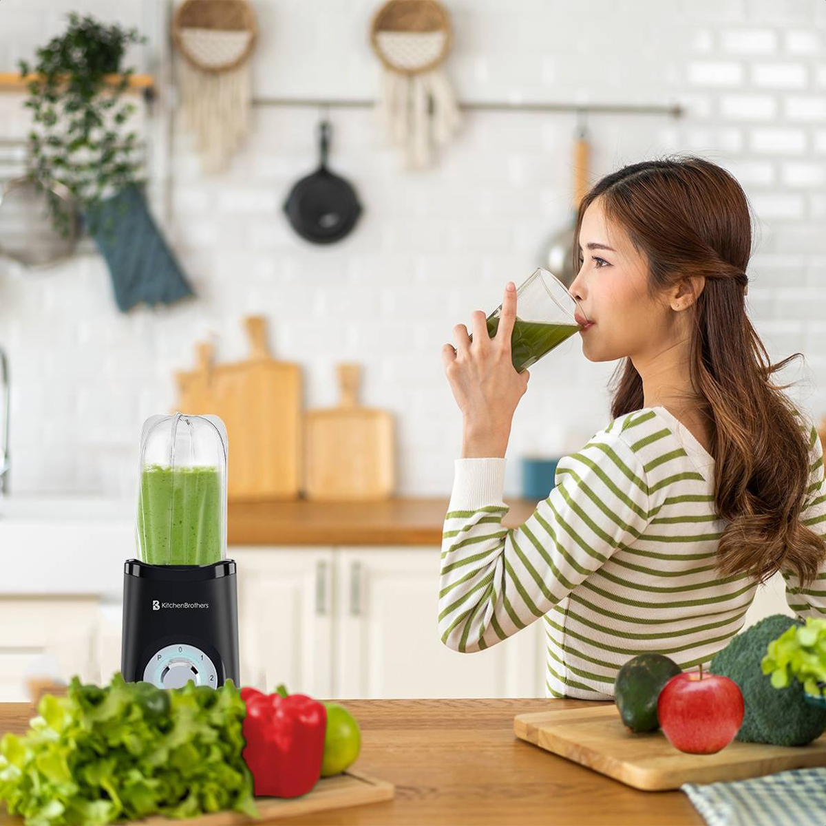 Woman drinking from a green smoothie, with blender on the counter. Vegetables and fruit are on the counter.