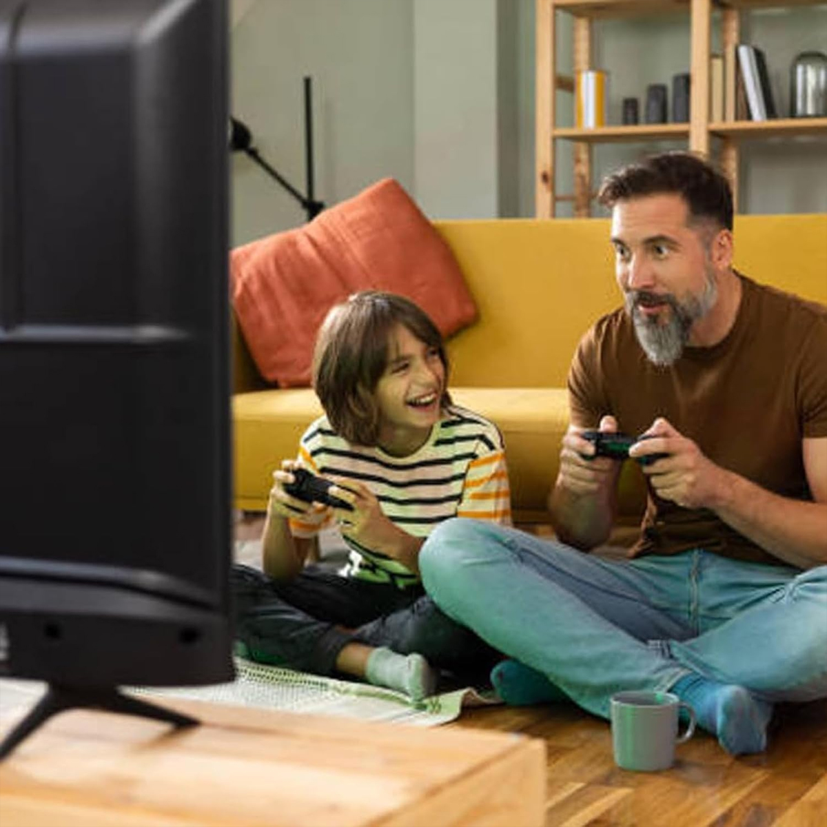 Padre e figlio giocano ai videogiochi. Divano giallo e TV sullo sfondo.