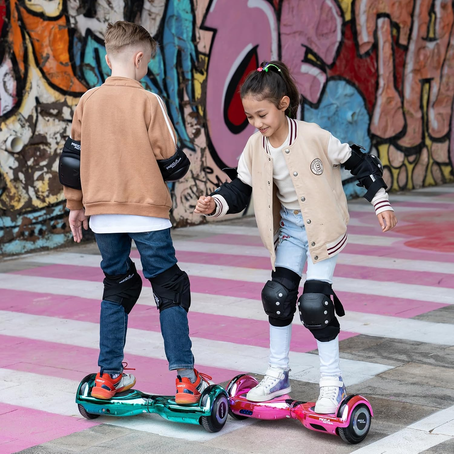 Dwoje dzieci na hoverboardach. Jedna dziewczyna. Oboje noszą sprzęt ochronny. Ściana graffiti w tle.