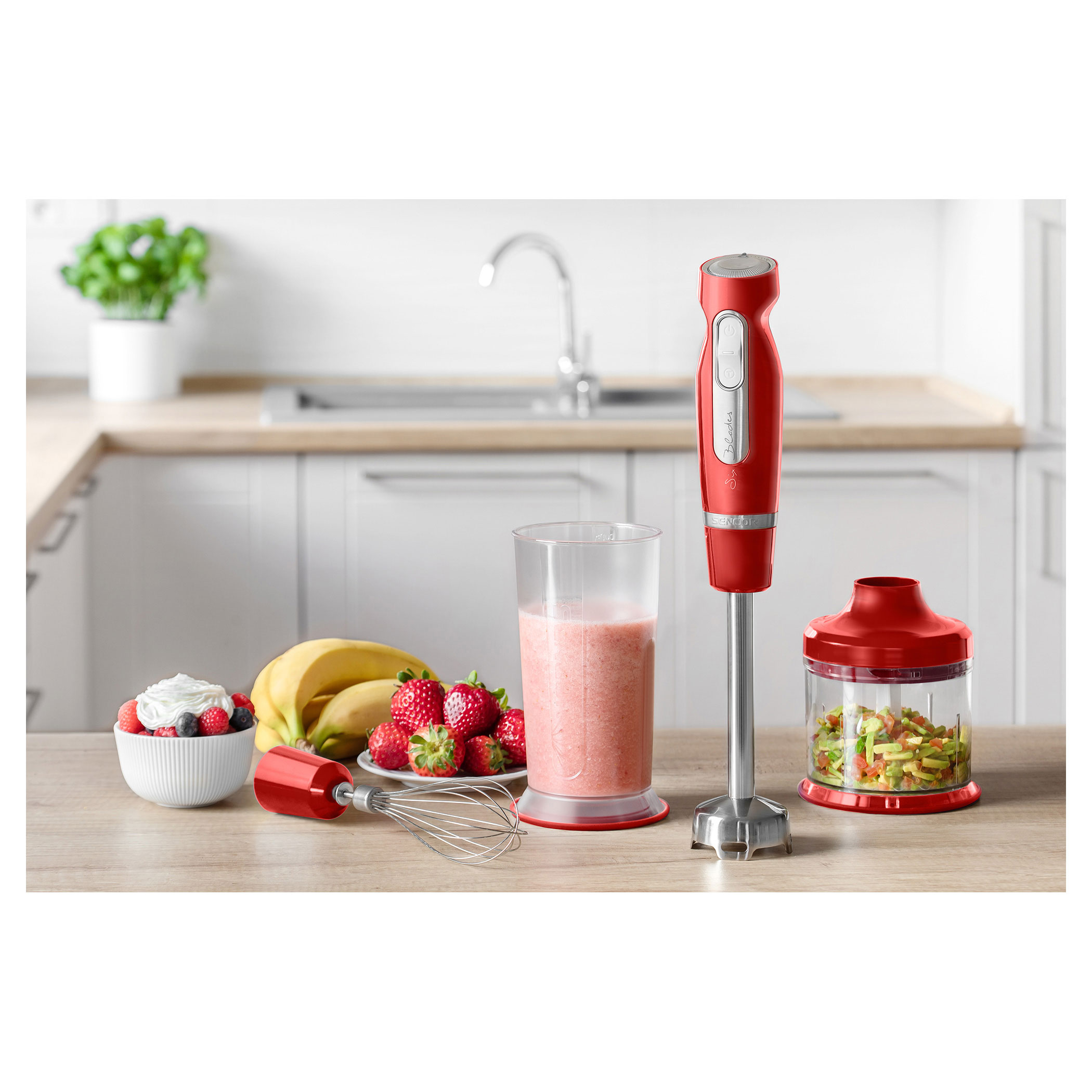 Czerwony blender ręczny z akcesoriami na drewnianym stole w kuchni.