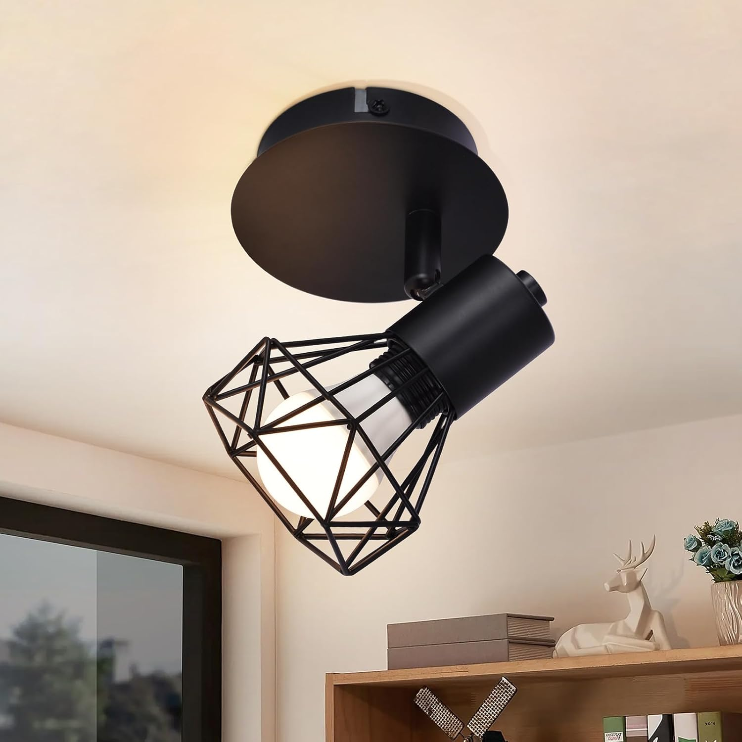 Lámpara de techo negra con pantalla tipo jaula, emitiendo luz. Ubicada en una habitación.