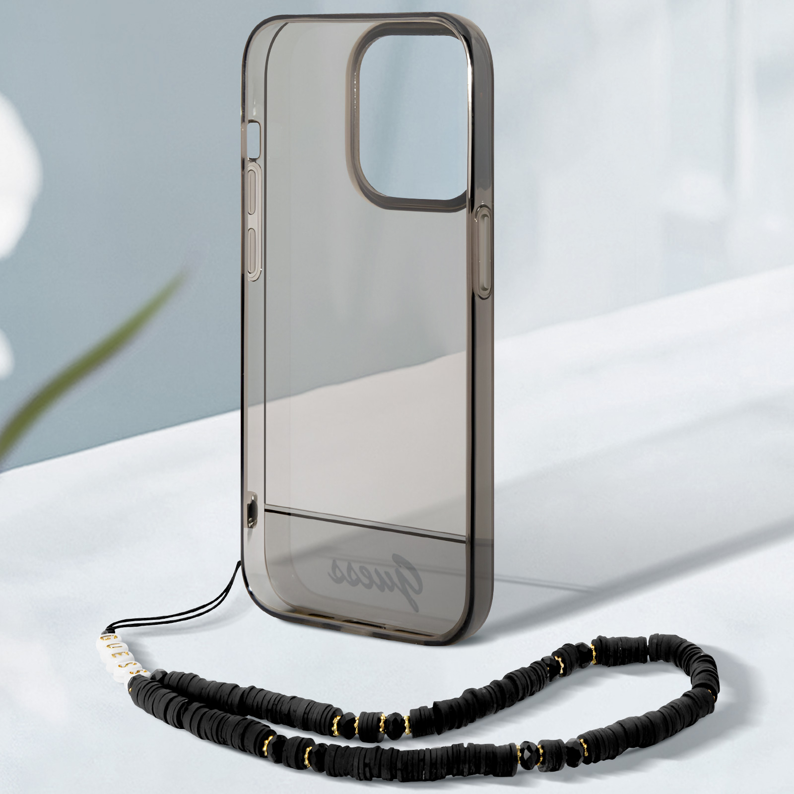 Custodia trasparente per telefono con cinturino nero. Accenti di colore nero e oro. La custodia poggia su una superficie.