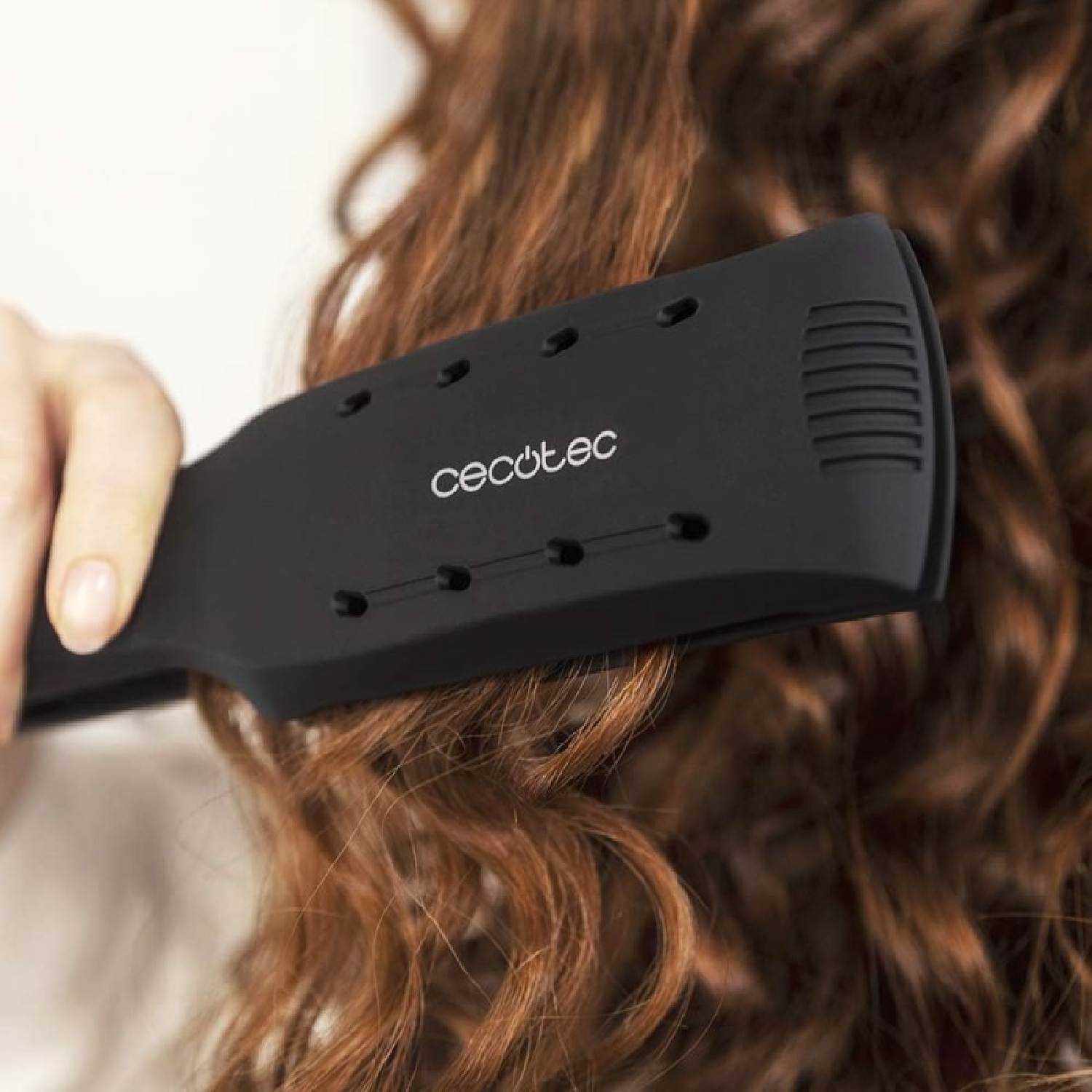 Una piastra nera viene utilizzata su capelli ricci rossi. Il dispositivo ha il marchio Cecotec.