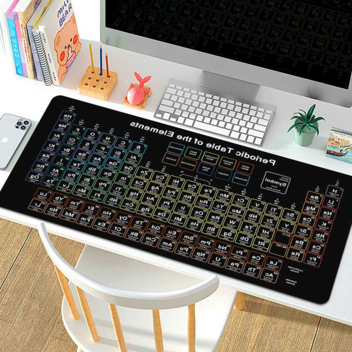 Periodieke tabel muismat op een wit bureau met computer, pennen en een plant.