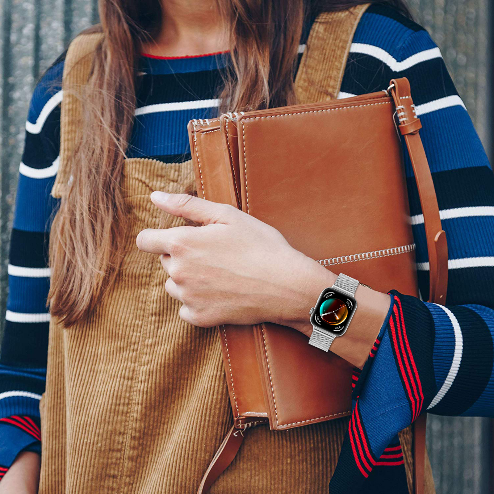 Kobieta nosząca smartwatch na nadgarstku, trzymająca brązową torebkę. Ma na sobie kombinezon.