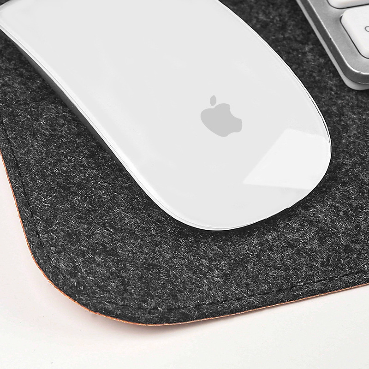 Mouse Apple bianco su un tappetino per mouse in feltro grigio scuro su una scrivania bianca.