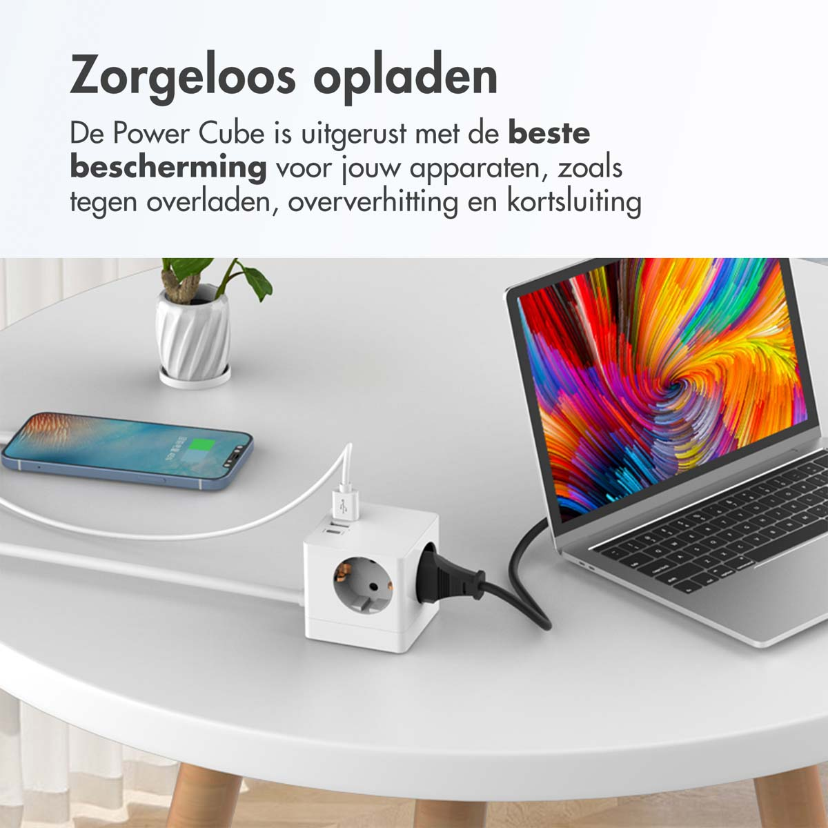 Witte power cube met een telefoon en laptop die op een tafel opladen. De scène is goed verlicht.