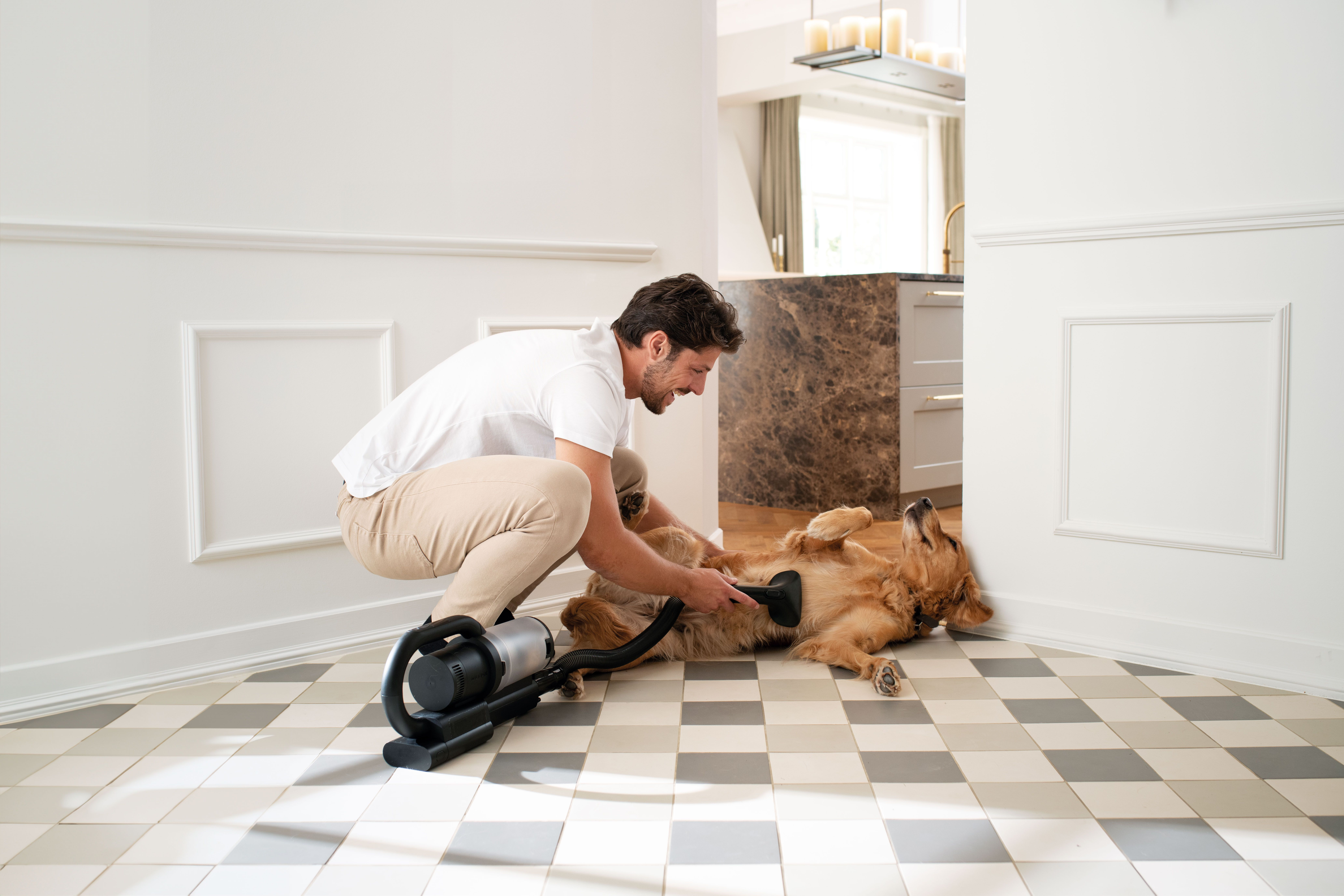 Adam beyaz duvarlı bir odada, yerde bir golden retriever cinsi köpeği süpürüyor.