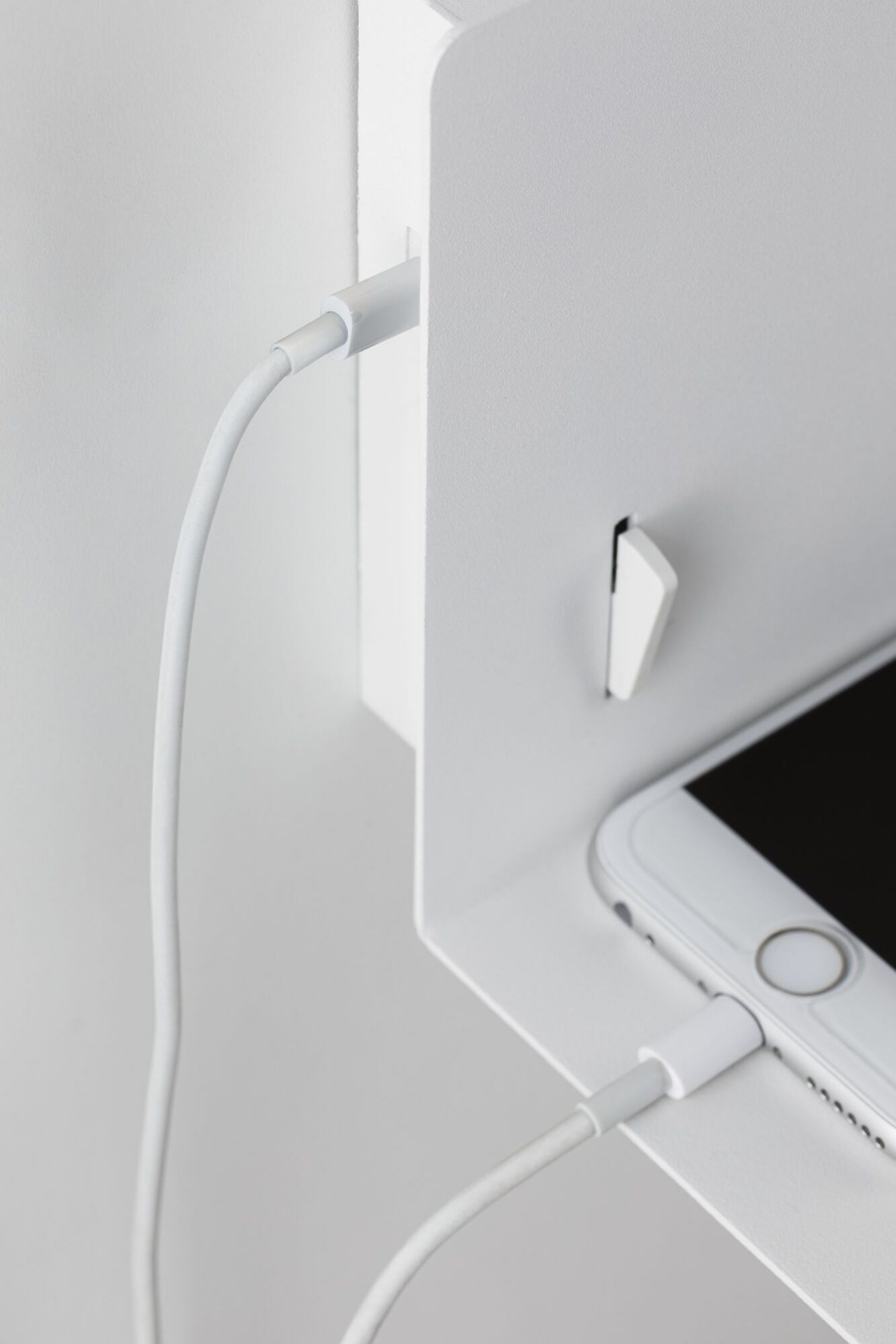 Weißes Regal mit ladendem weißen Telefon. Ein weißes Kabel ist mit dem Telefon und dem Regal verbunden.