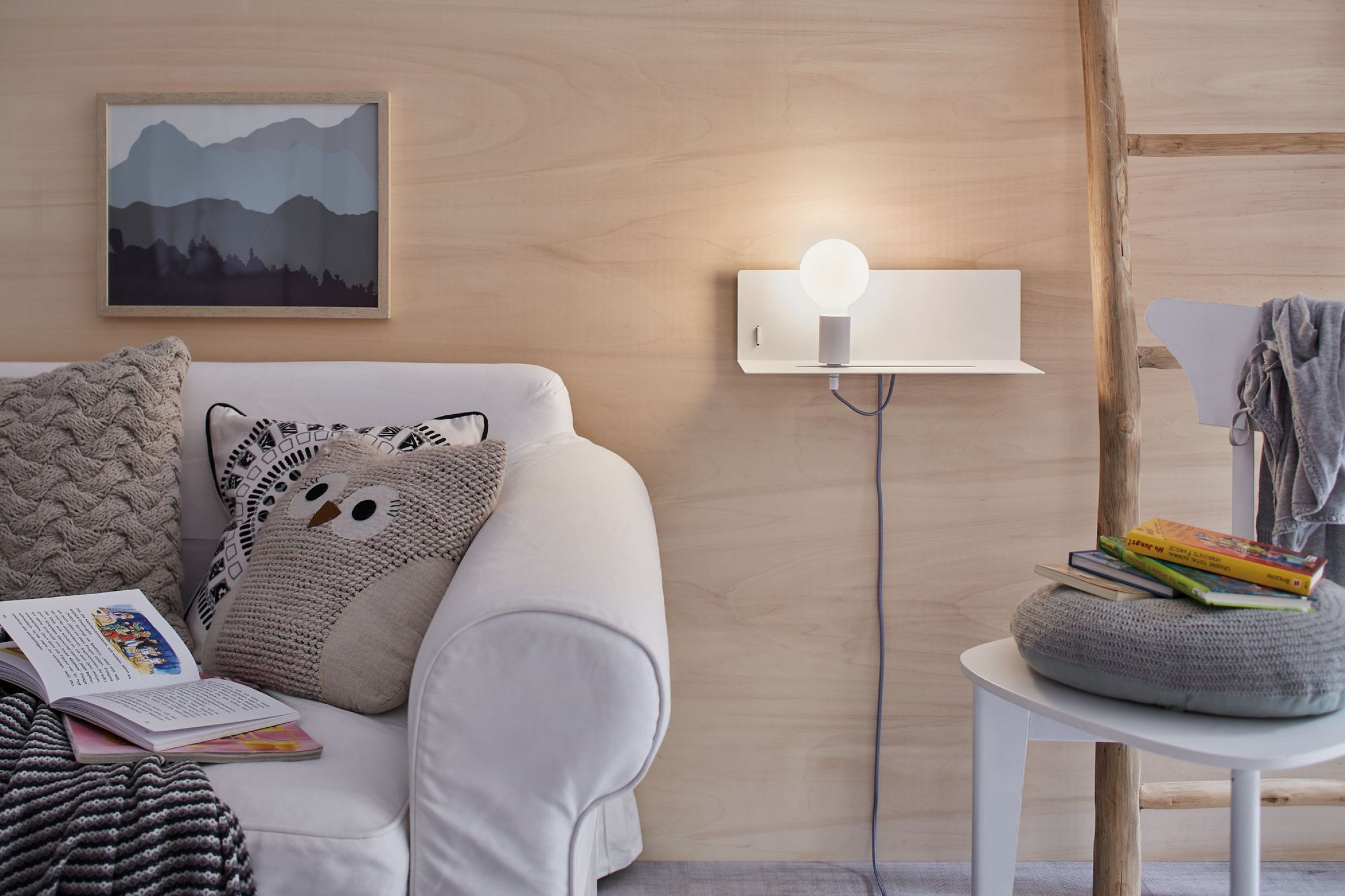 Biała sofa, poduszka i lampa ścienna z żarówką na drewnianej ścianie.