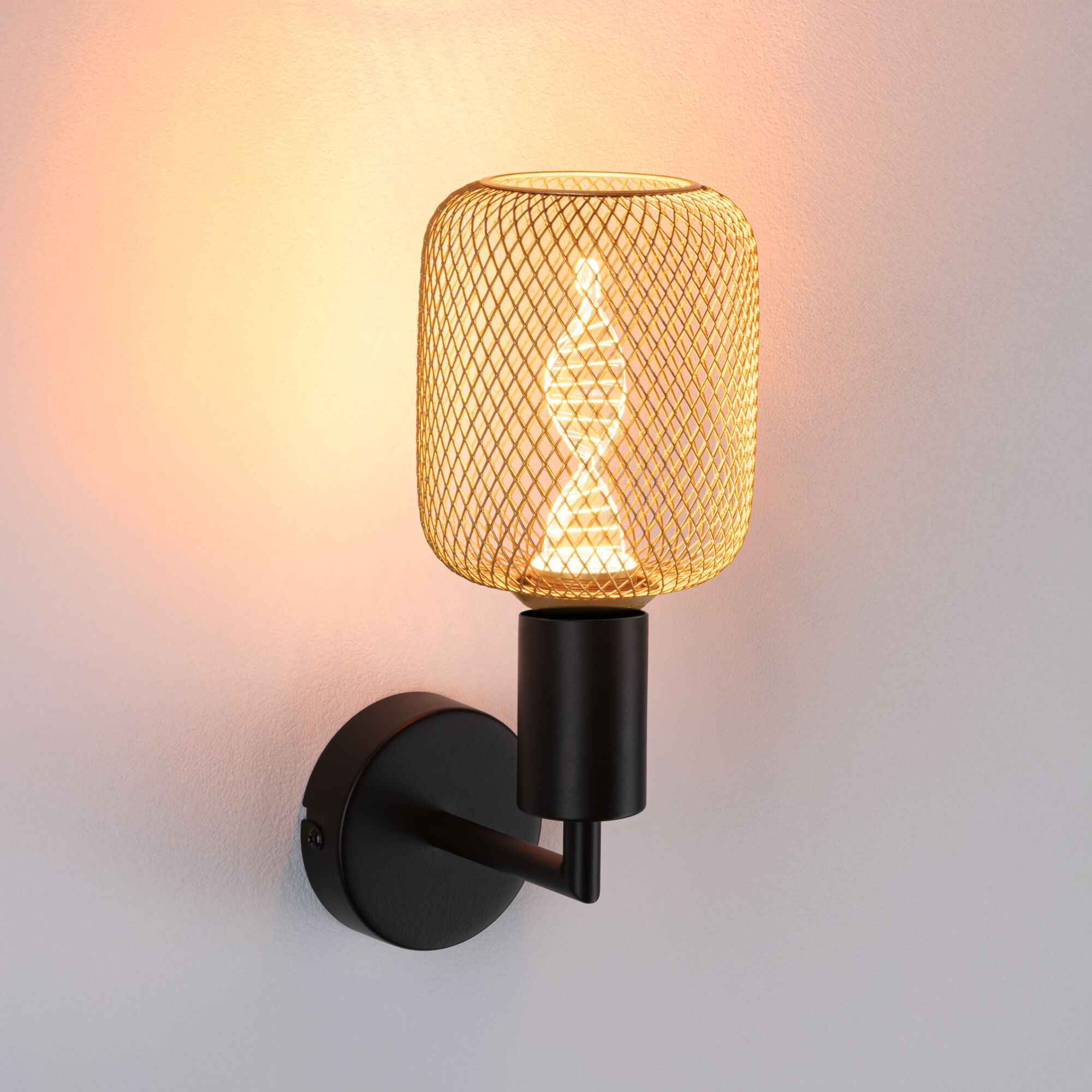 Eine goldene Drahtlampe an einem schwarzen Ständer, der an einer weißen Wand befestigt ist.