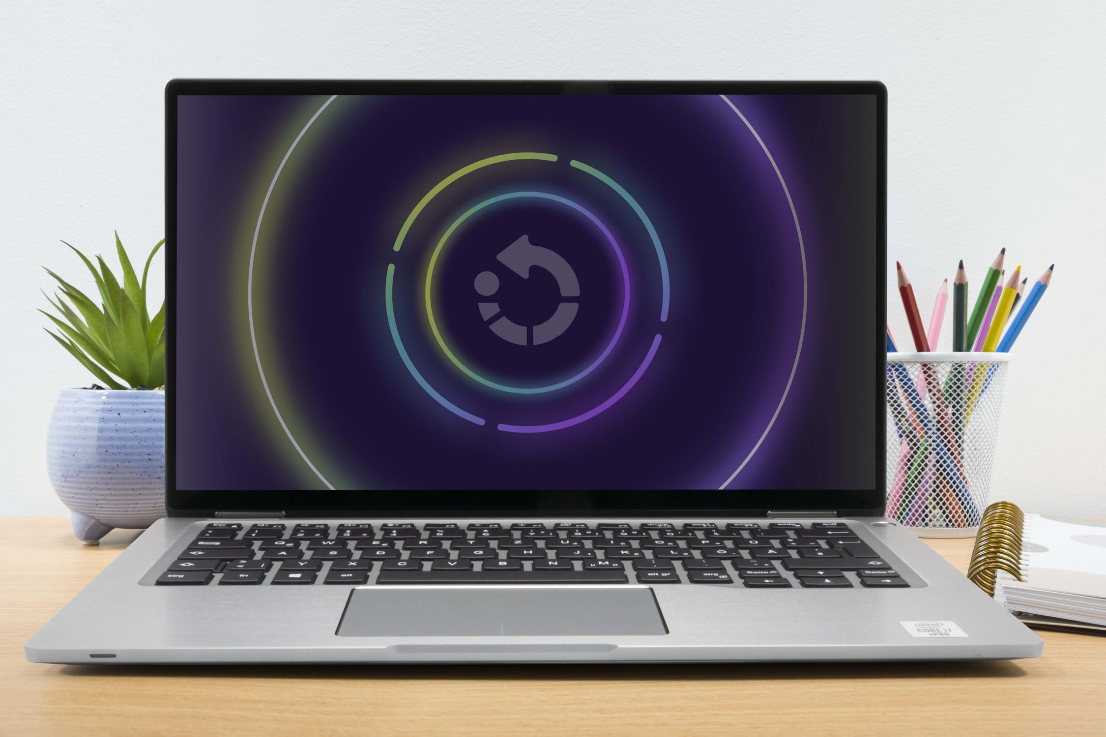 Laptop-Bildschirm mit bunter Grafik sowie eine Pflanze und Stifte auf dem Schreibtisch. Weißer Hintergrund.