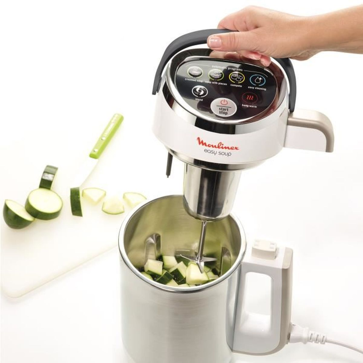 Una donna tiene un'apparecchio per zuppa bianco e argento. Zucchine su tagliere.