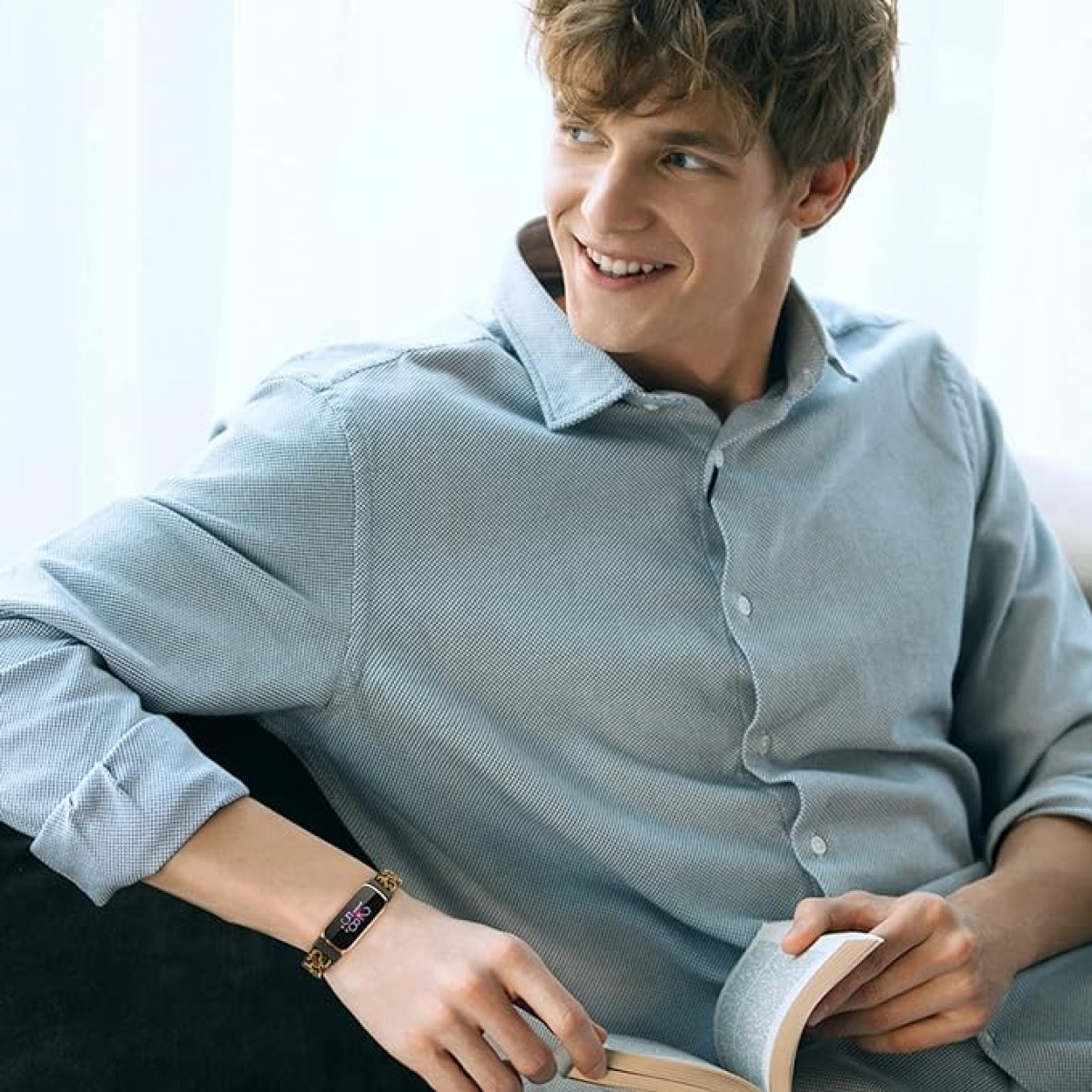 Mężczyzna z opaską fitness na lewym nadgarstku, siedzący, trzymający książkę i uśmiechający się do kamery.