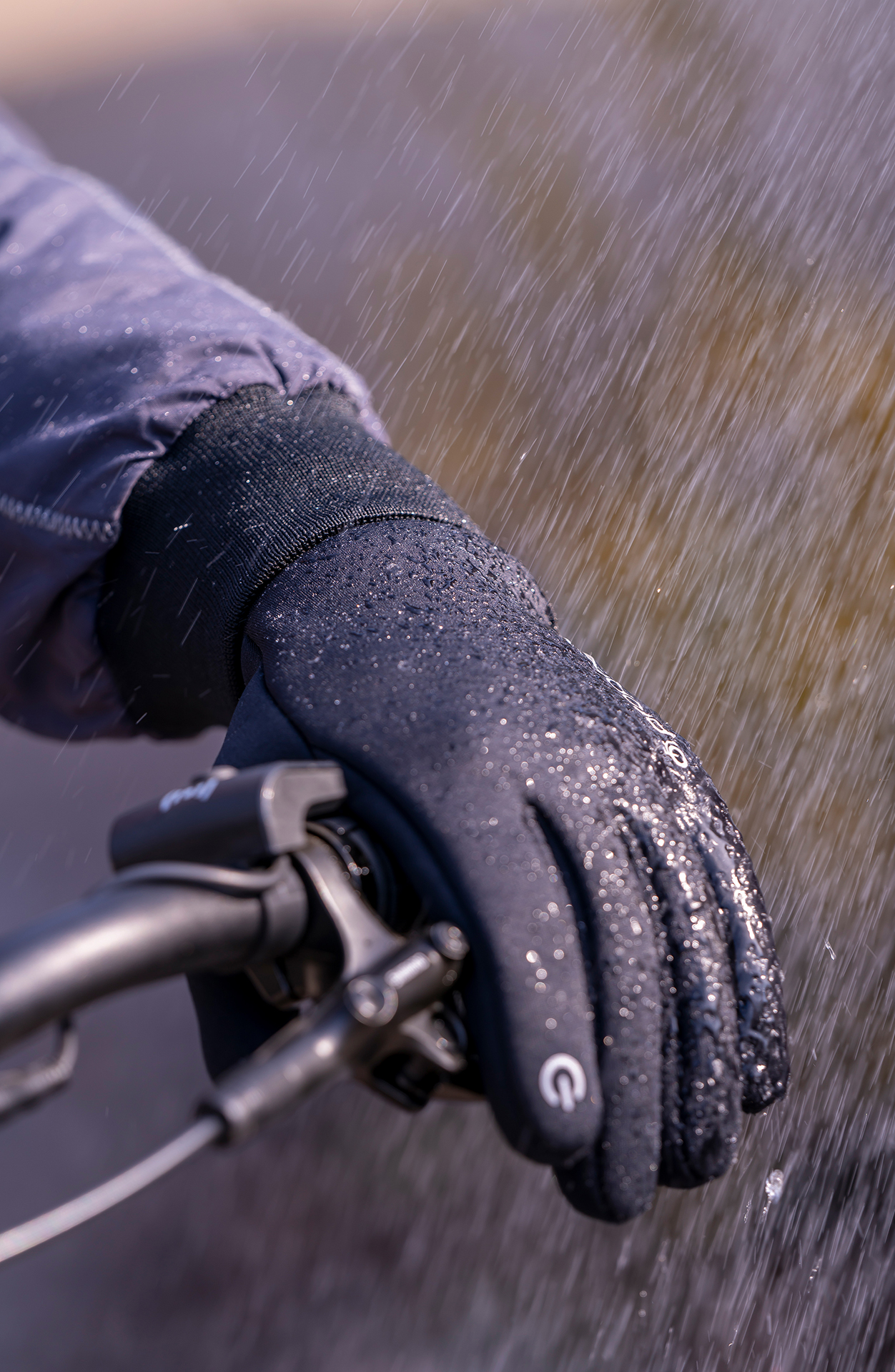 Eine behandschuhte Hand an einem Fahrradlenker, es regnet. Die Hand ist schwarz und nass.