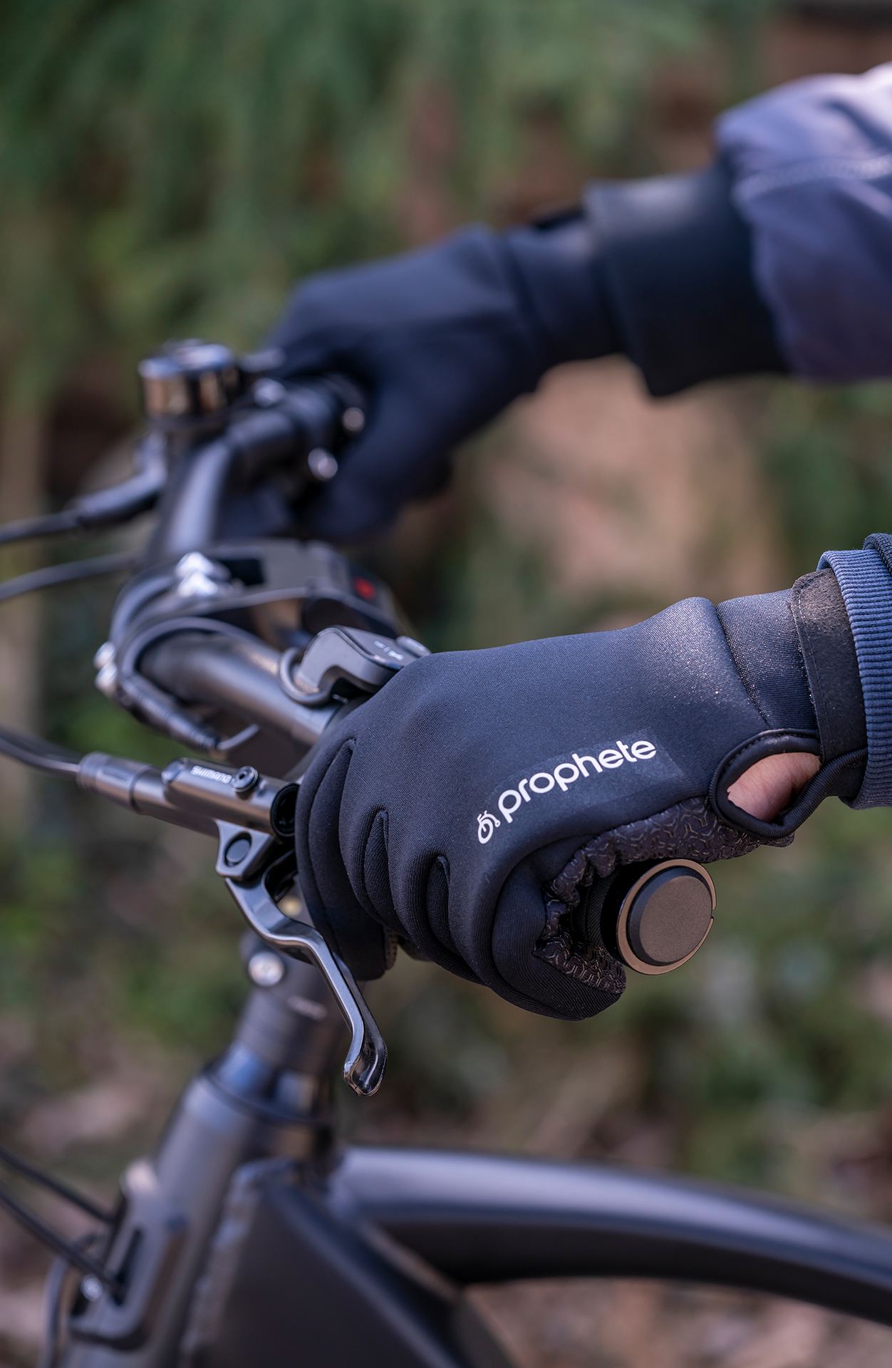 Hände mit schwarzen Handschuhen an einem Fahrradlenker, mit der Marke 'Prophete'.