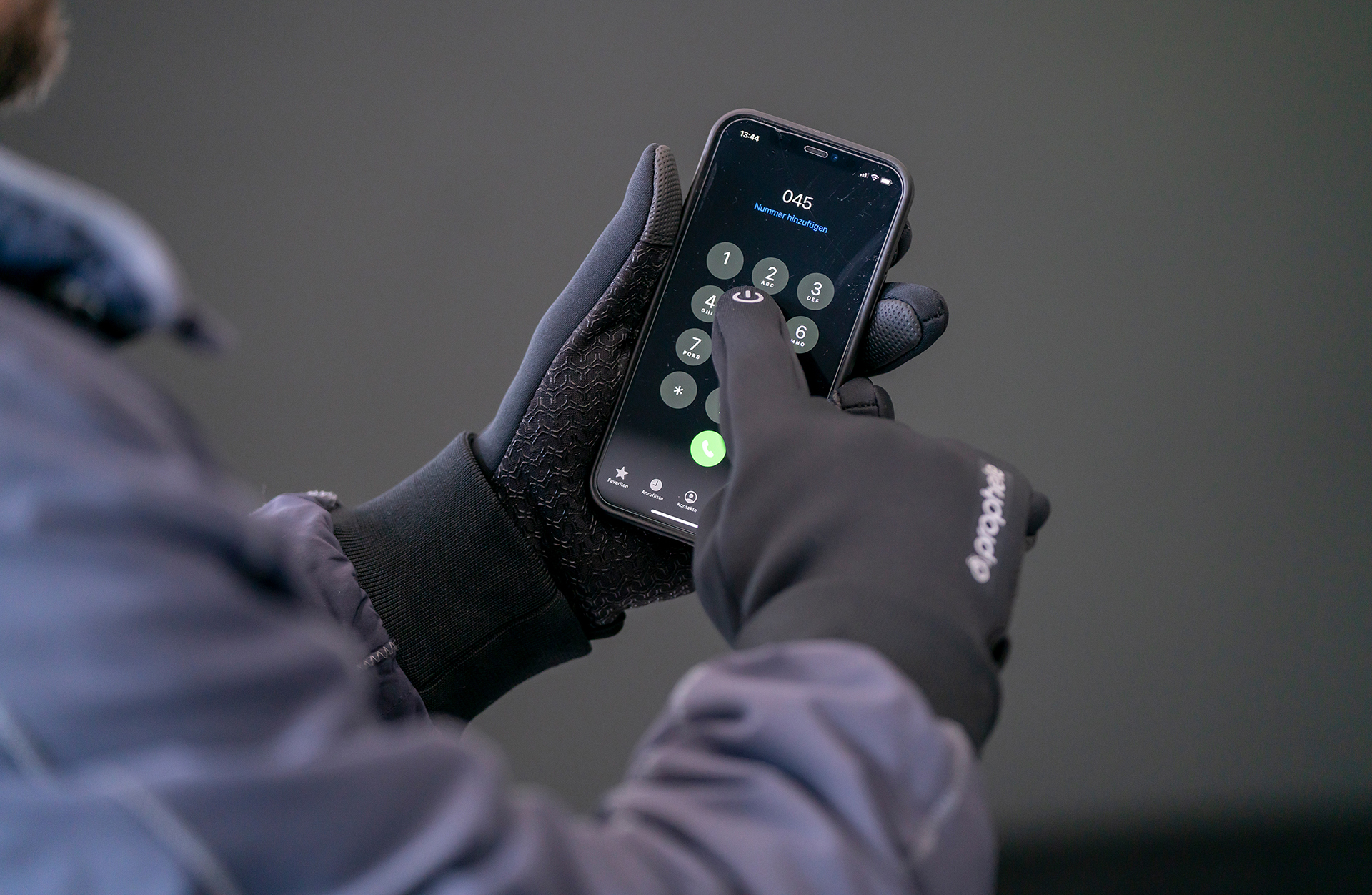 Person mit Handschuhen wählt eine Nummer auf dem Smartphone-Bildschirm.