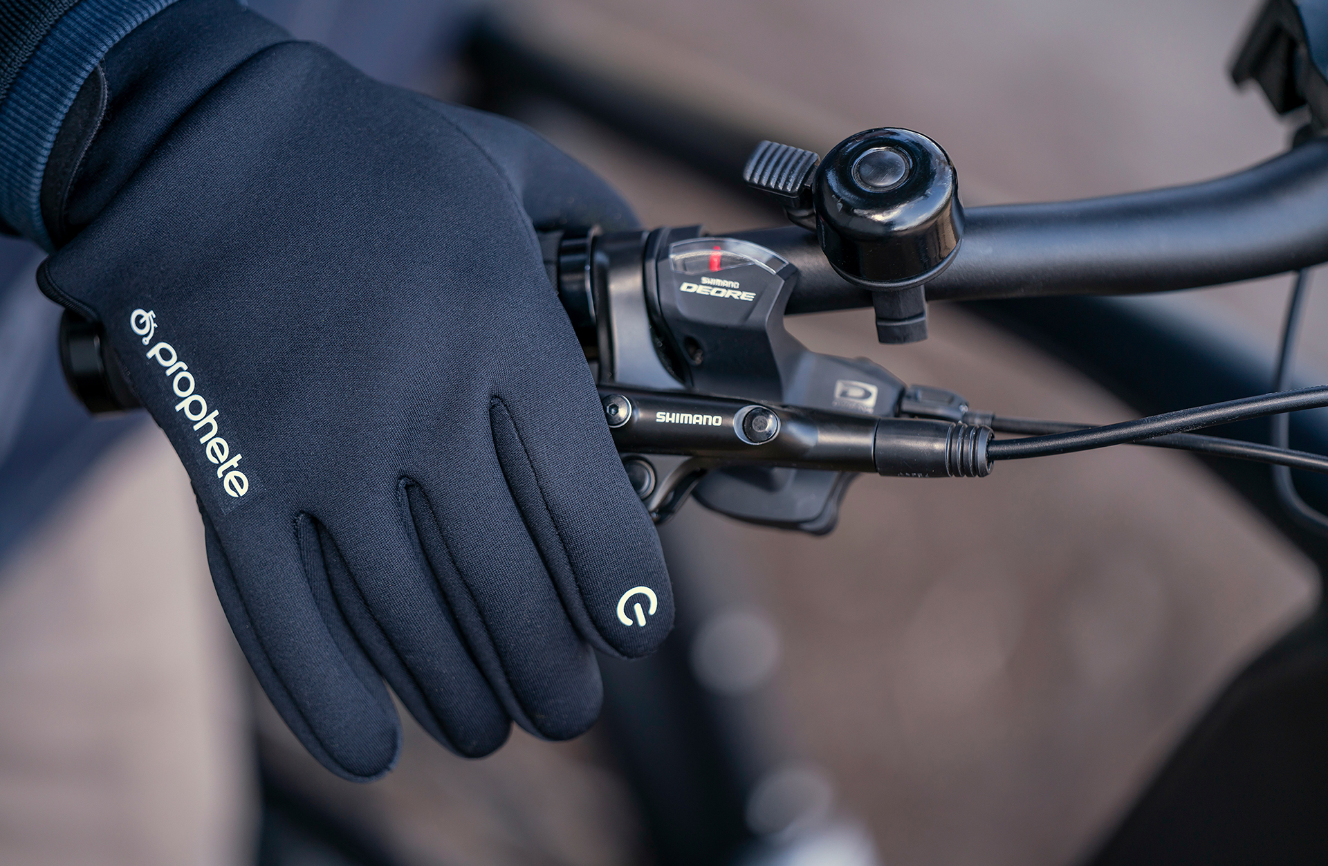 Die Hand einer Person, die einen Fahrradlenker mit schwarzen Handschuhen hält.