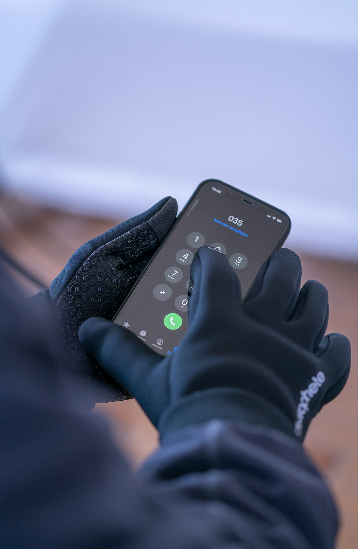 Eine Person mit schwarzen Handschuhen hält ein Telefon. Das Telefon zeigt eine Tastatur mit einer Ruftaste.