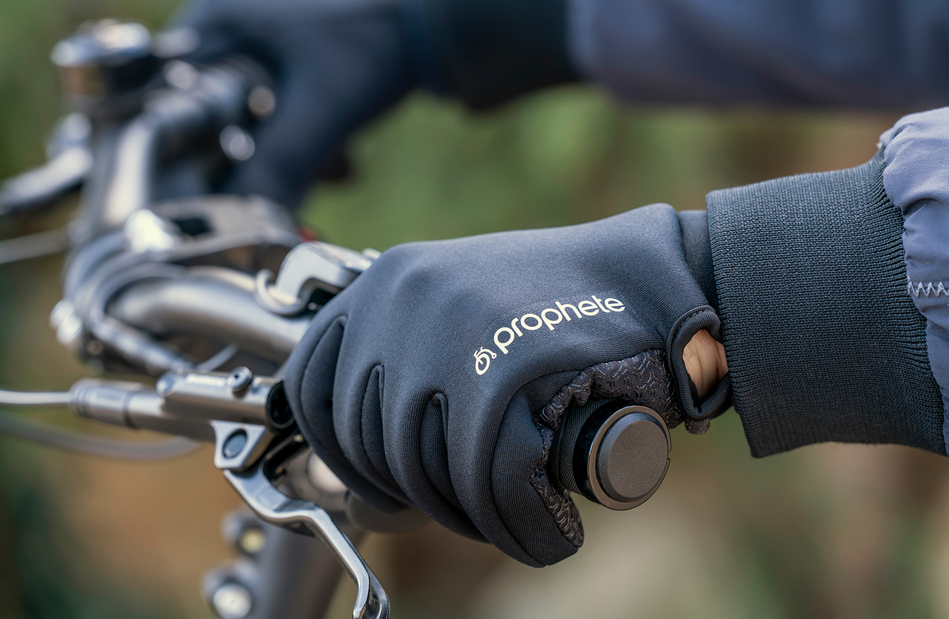 Schwarze Handschuhe an Fahrradlenkern. Weißes Prophete-Logo. Dunkler Hintergrund.