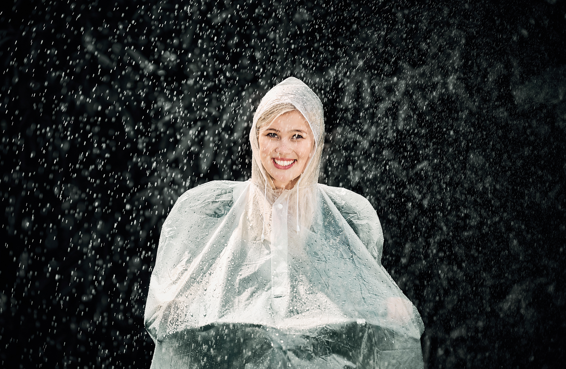 Frau in einem transparenten Regenmantel, die im Regen lächelt.
