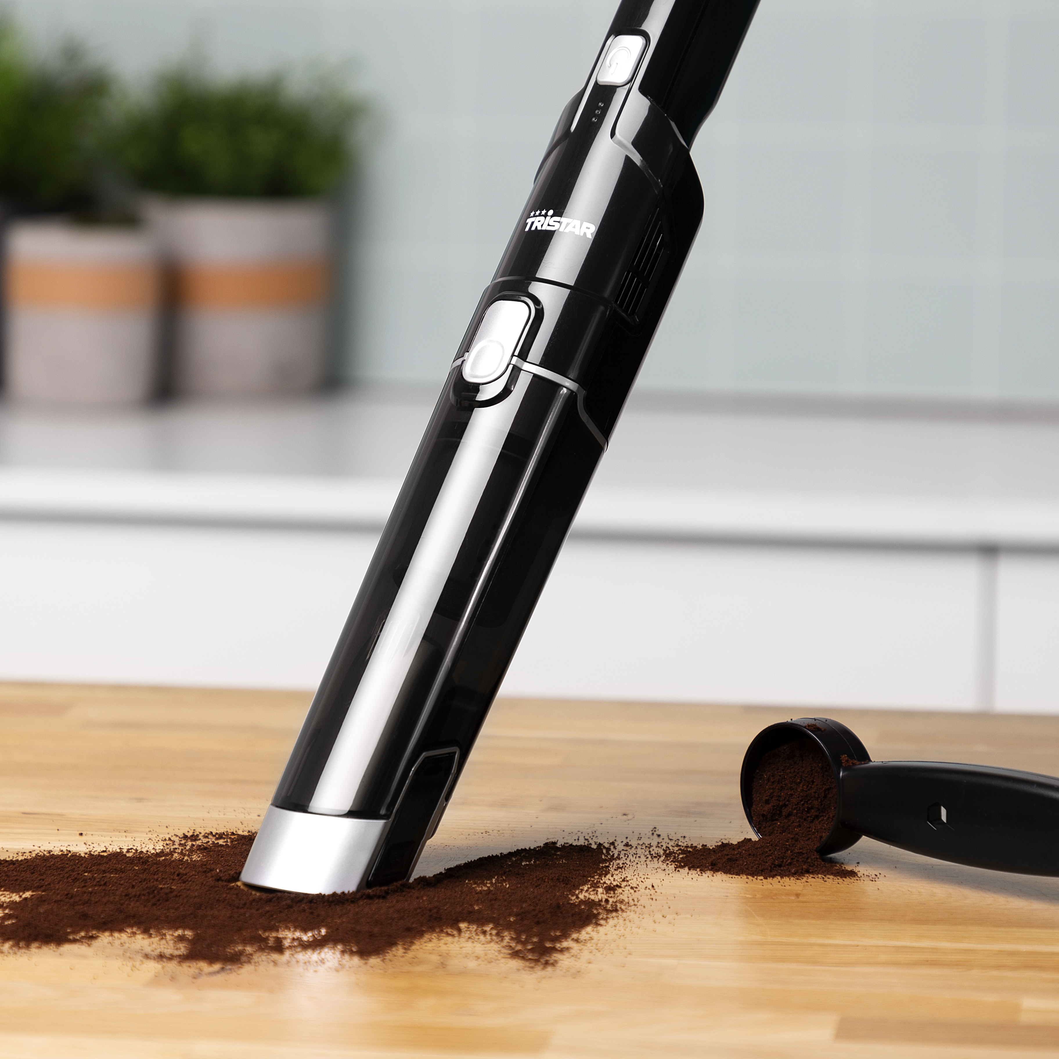 Aspirapolvere portatile nero su una superficie di legno, che aspira fondi di caffè da un cucchiaino.
