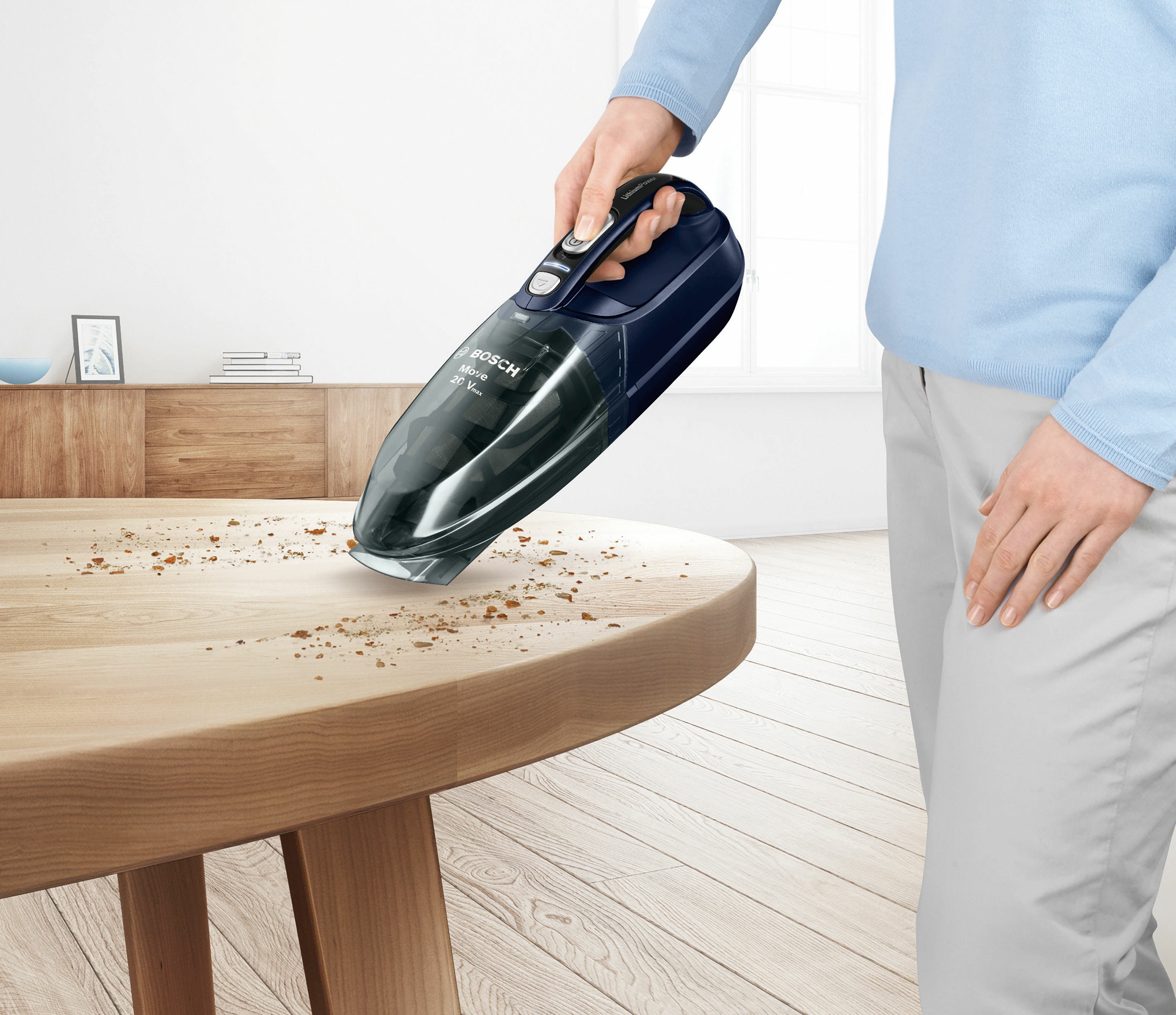 Una persona usa una pequeña aspiradora de mano sobre una mesa de madera, limpiando migas.
