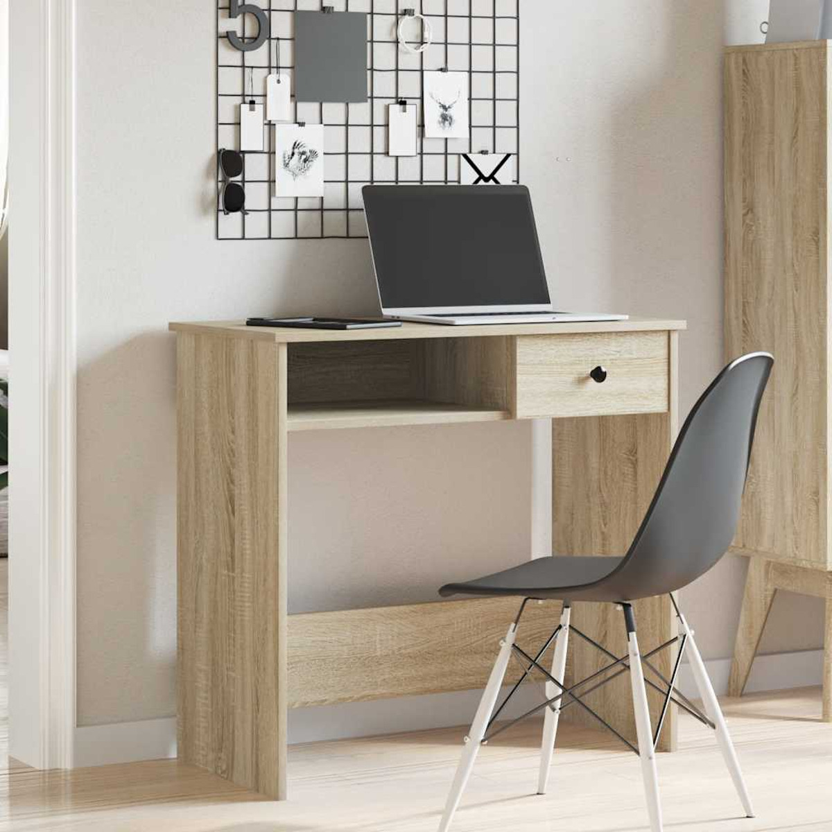 Holzschreibtisch mit Laptop, Schublade und Stuhl. Gitter mit Notizen an der Wand.