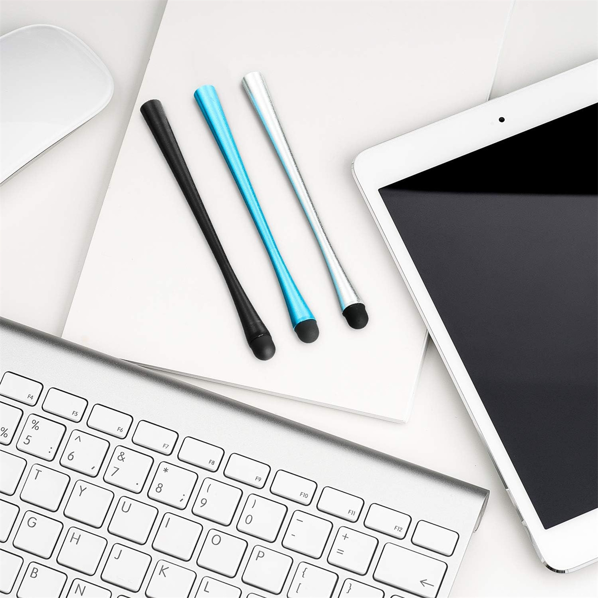 Eine Tastatur, ein Tablet und drei farbige Stifte auf einer weißen Oberfläche. Der Hintergrund ist weiß.