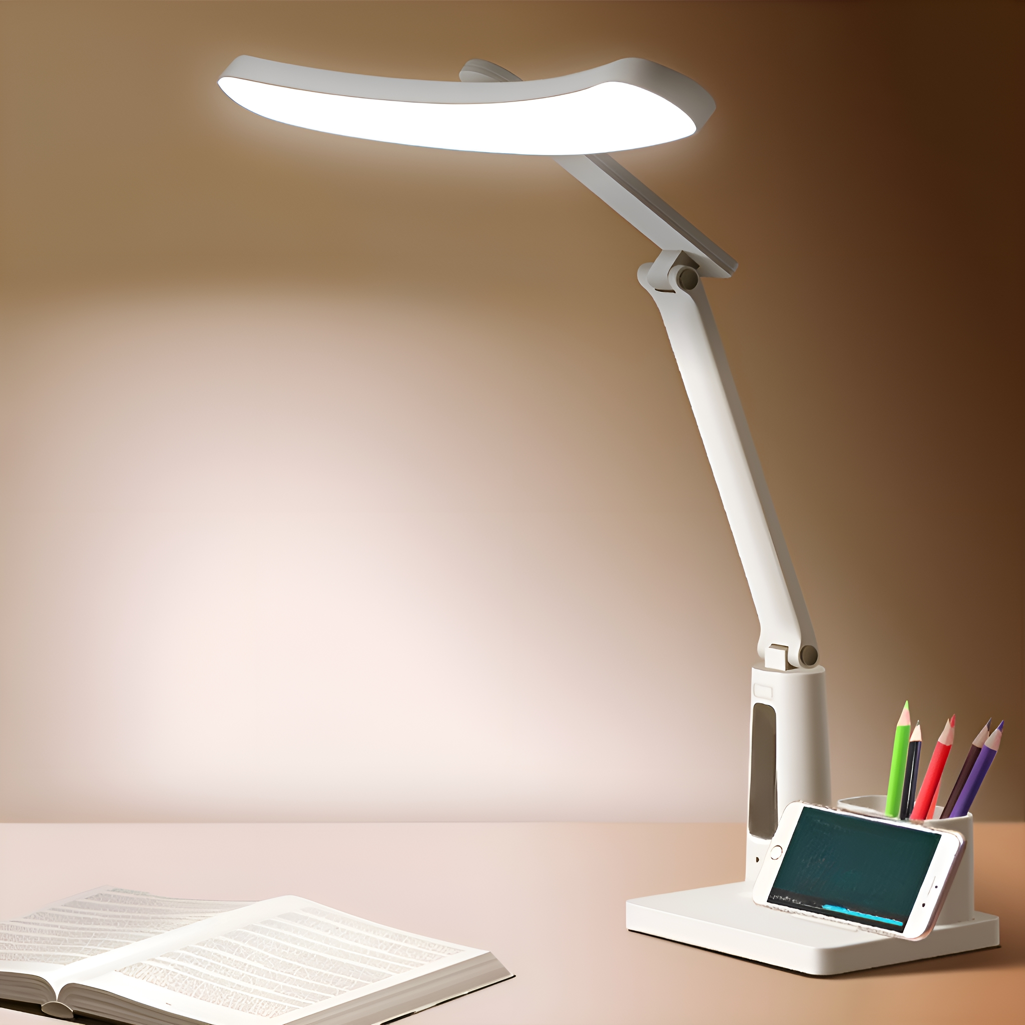 Eine weiße Schreibtischlampe mit Telefonhalter. Die Lampe steht auf einem Schreibtisch mit einem Buch und Stiften.