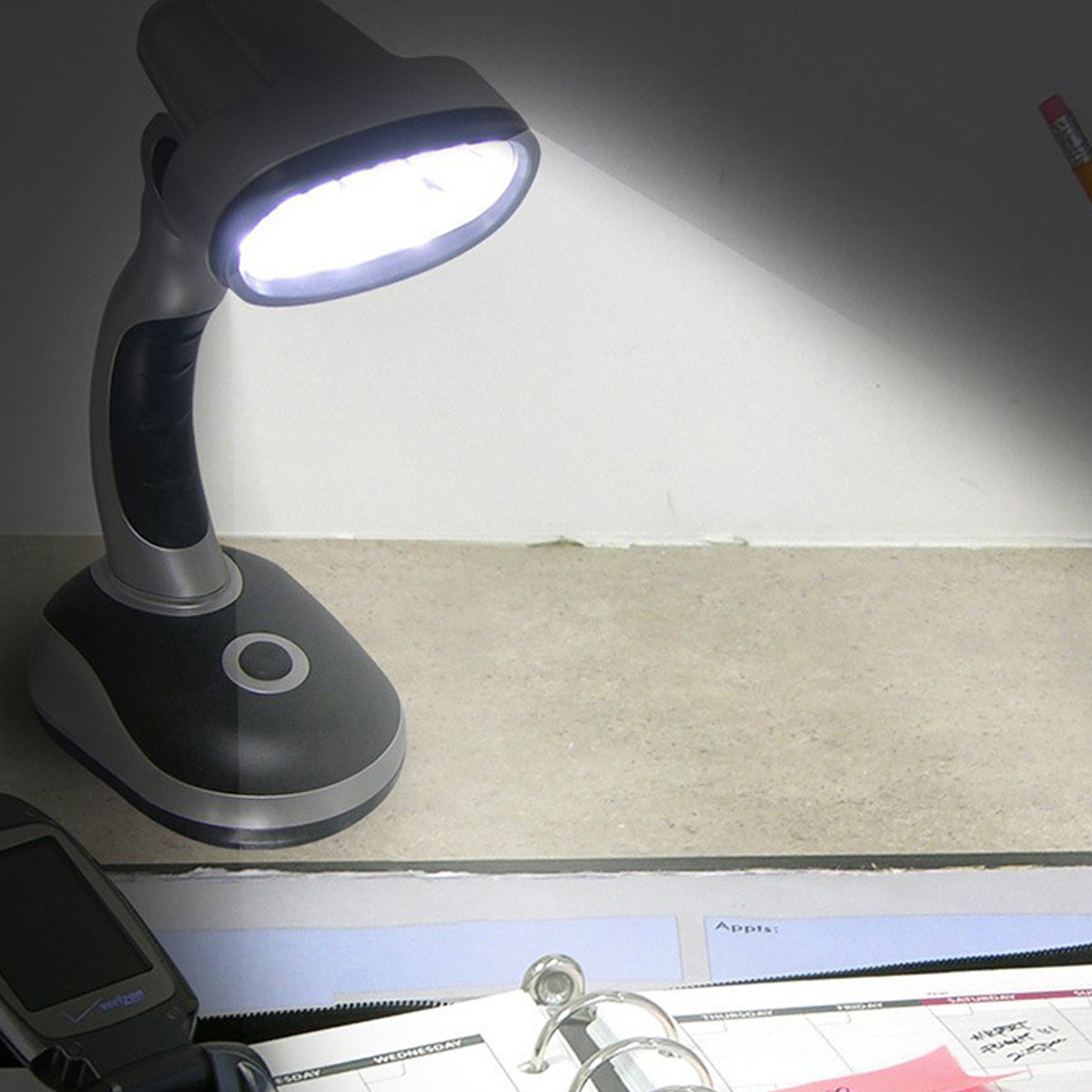 Eine Schreibtischlampe, die Licht auf einen Schreibtisch mit Kalender und Telefon abstrahlt.