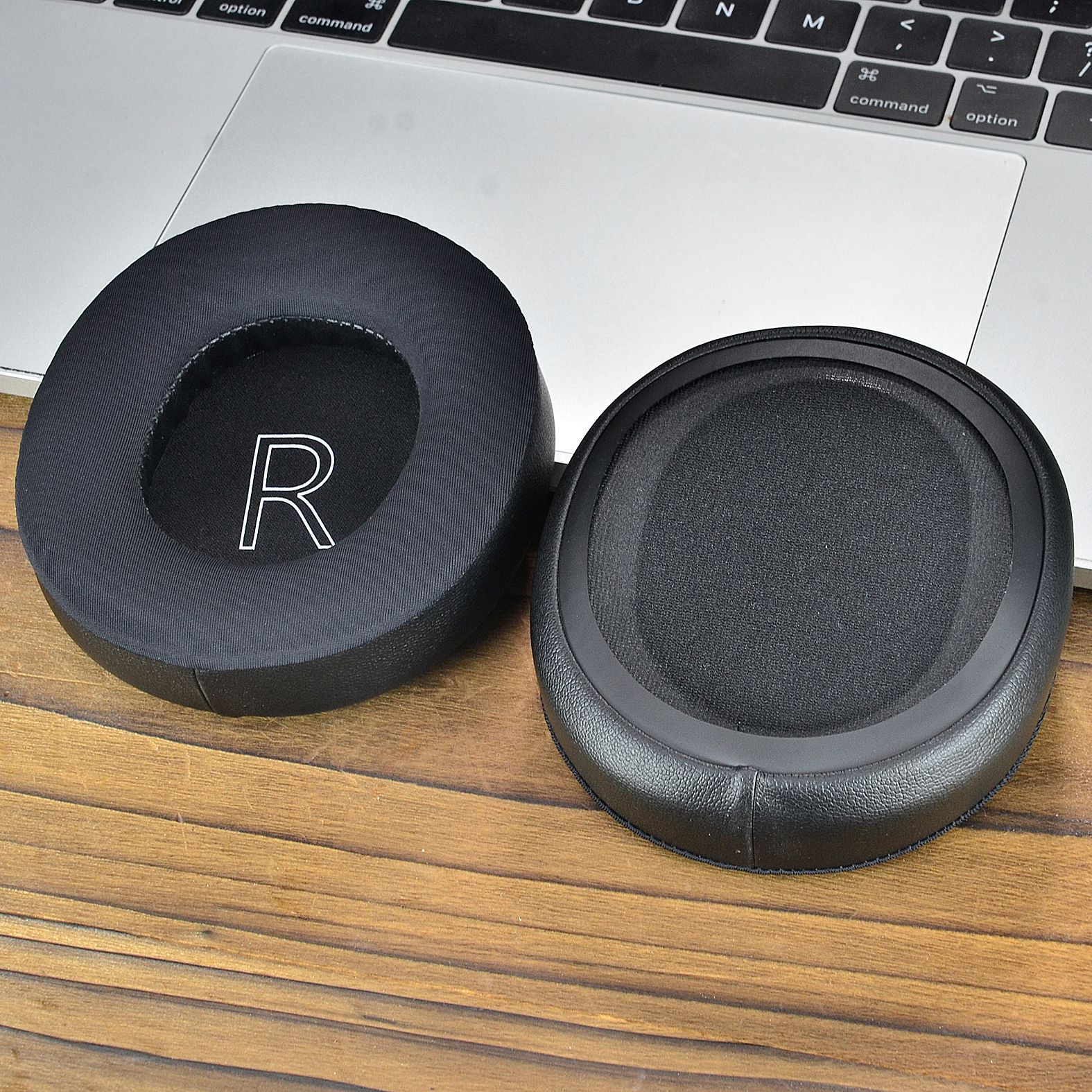 Dwie czarne nausznice słuchawek, jedna z nadrukowaną literą "R", spoczywające na klawiaturze laptopa.
