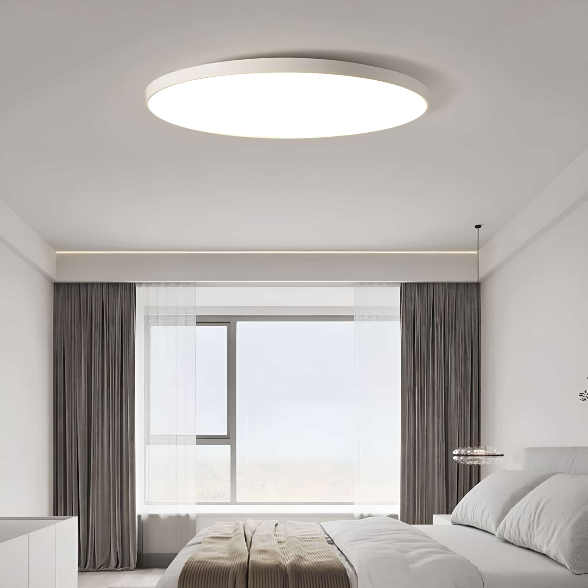 Eine runde, weiße Deckenleuchte in einem Schlafzimmer. Das Zimmer hat ein Fenster und Vorhänge.
