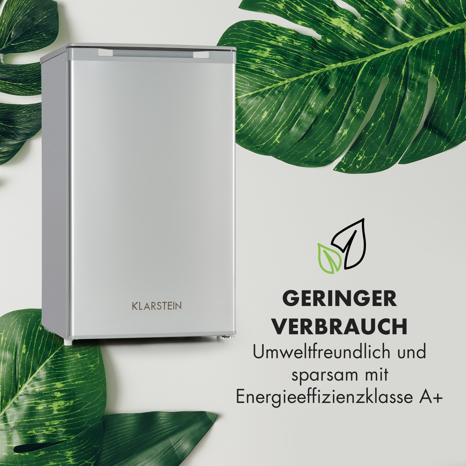 Silberner Mini-Kühlschrank, umgeben von grünen Blättern. Text auf der Seite.