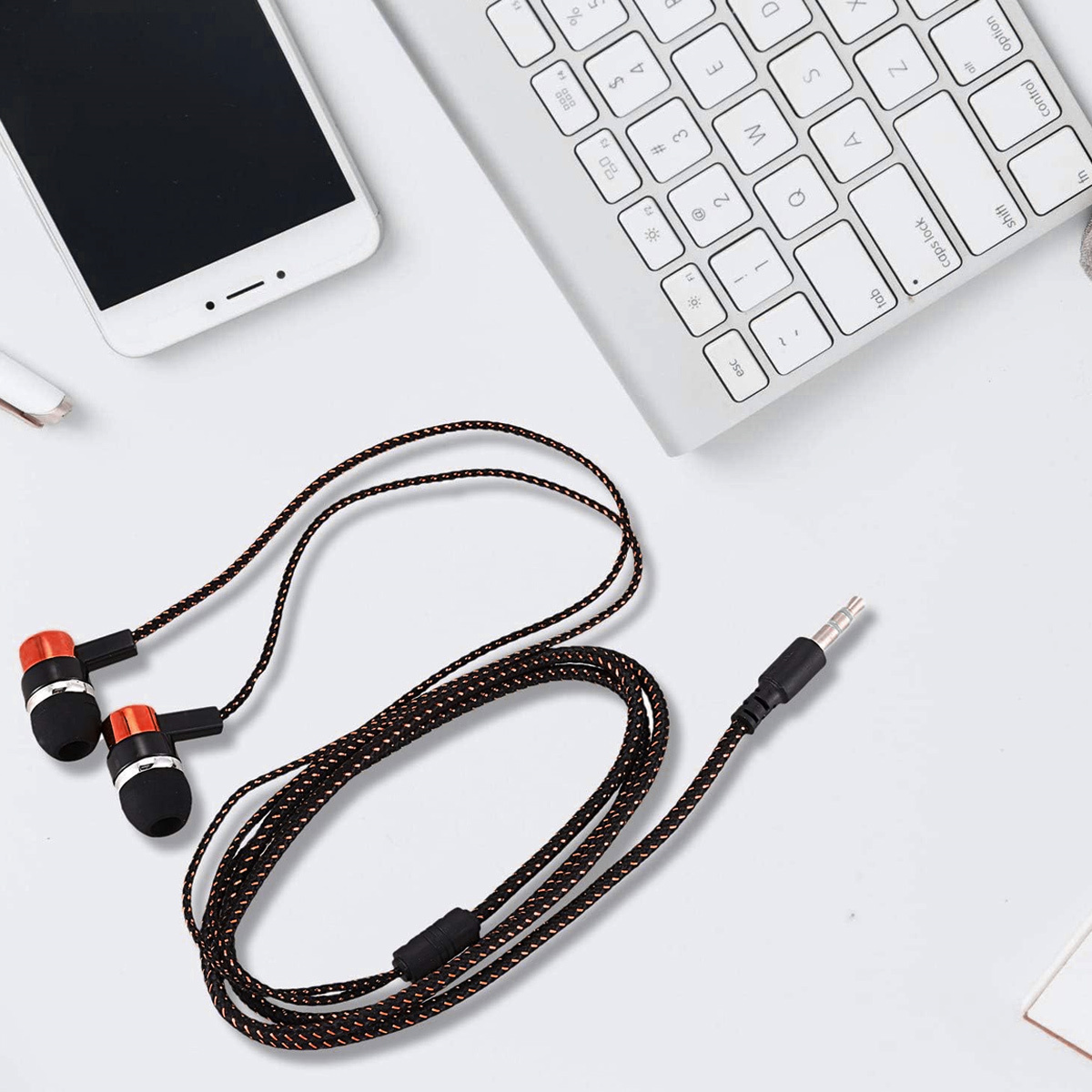 Kopfhörer mit orangefarbenen Ohrtips und schwarz-orange geflochtenem Kabel, weißes Telefon und Tastatur.