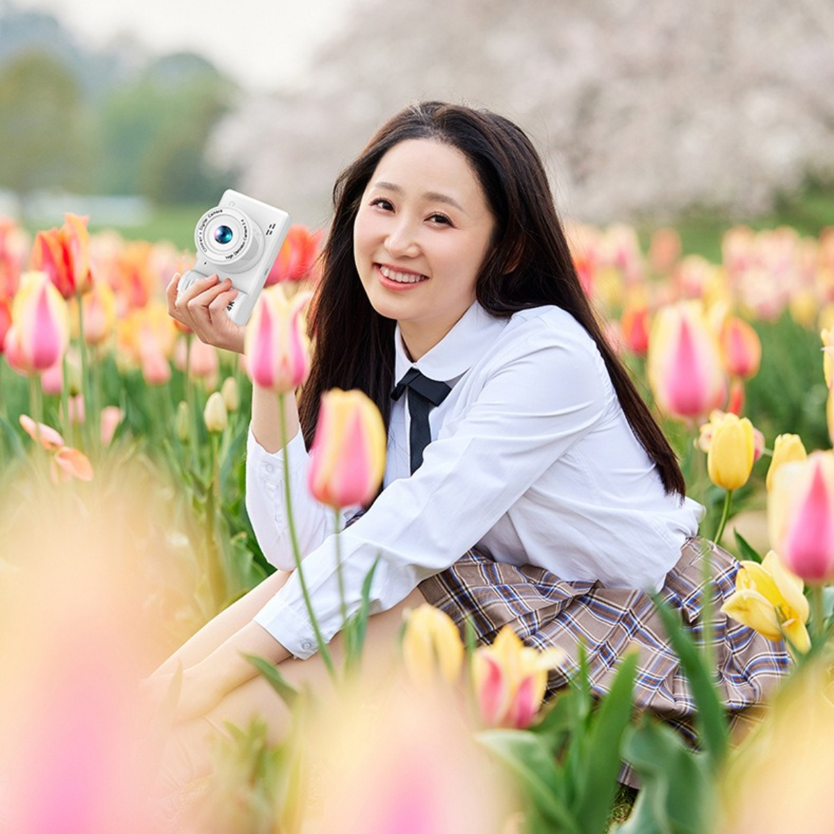 Eine lächelnde Frau hält eine weiße Kamera in einem Feld bunter Tulpen.