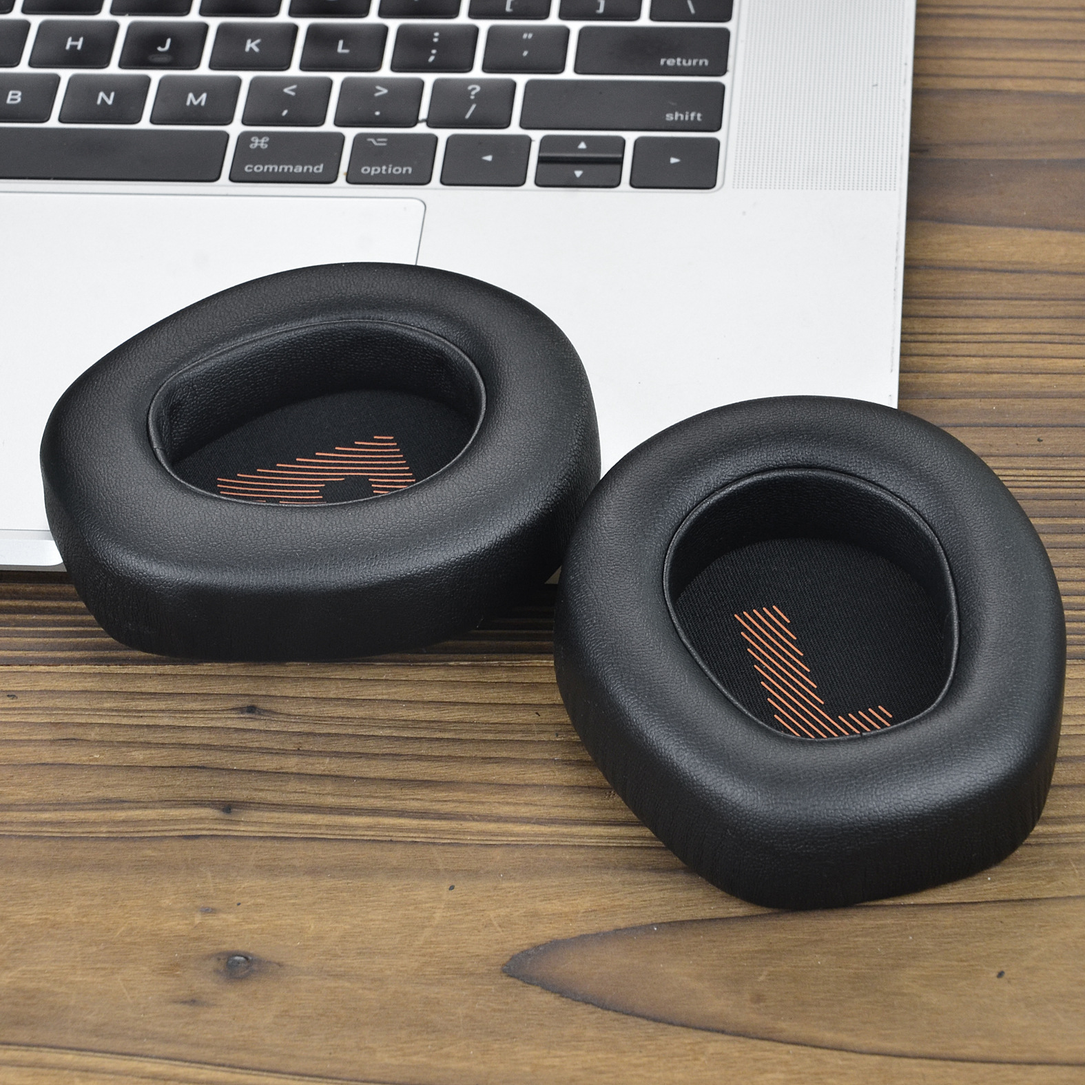 Dwie czarne, okrągłe poduszki na uszy do słuchawek spoczywają na srebrnej klawiaturze laptopa.
