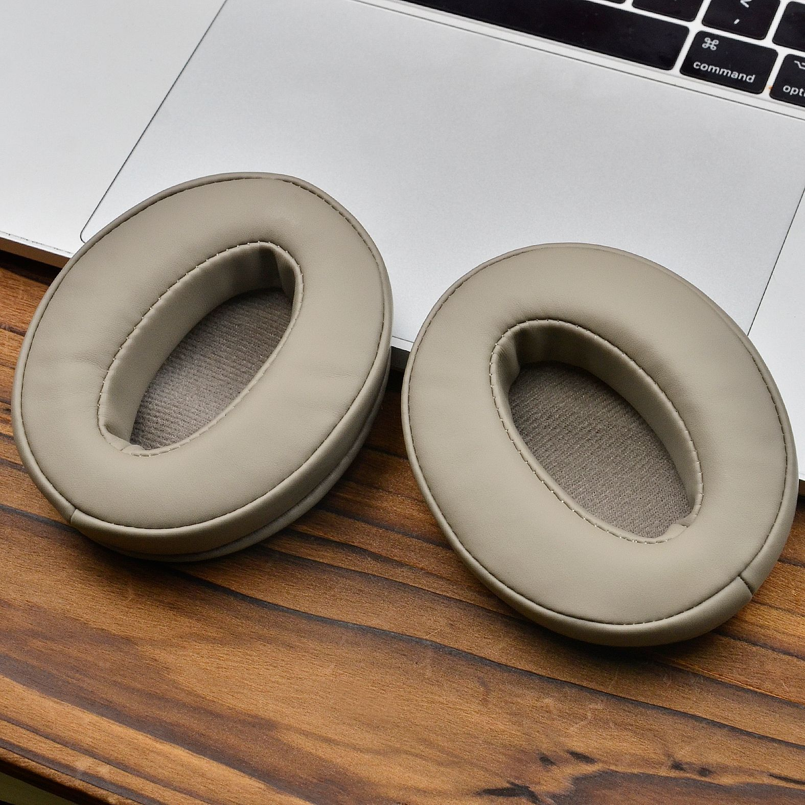 Twee beige oorkussens voor een koptelefoon op een laptoptoetsenbord.