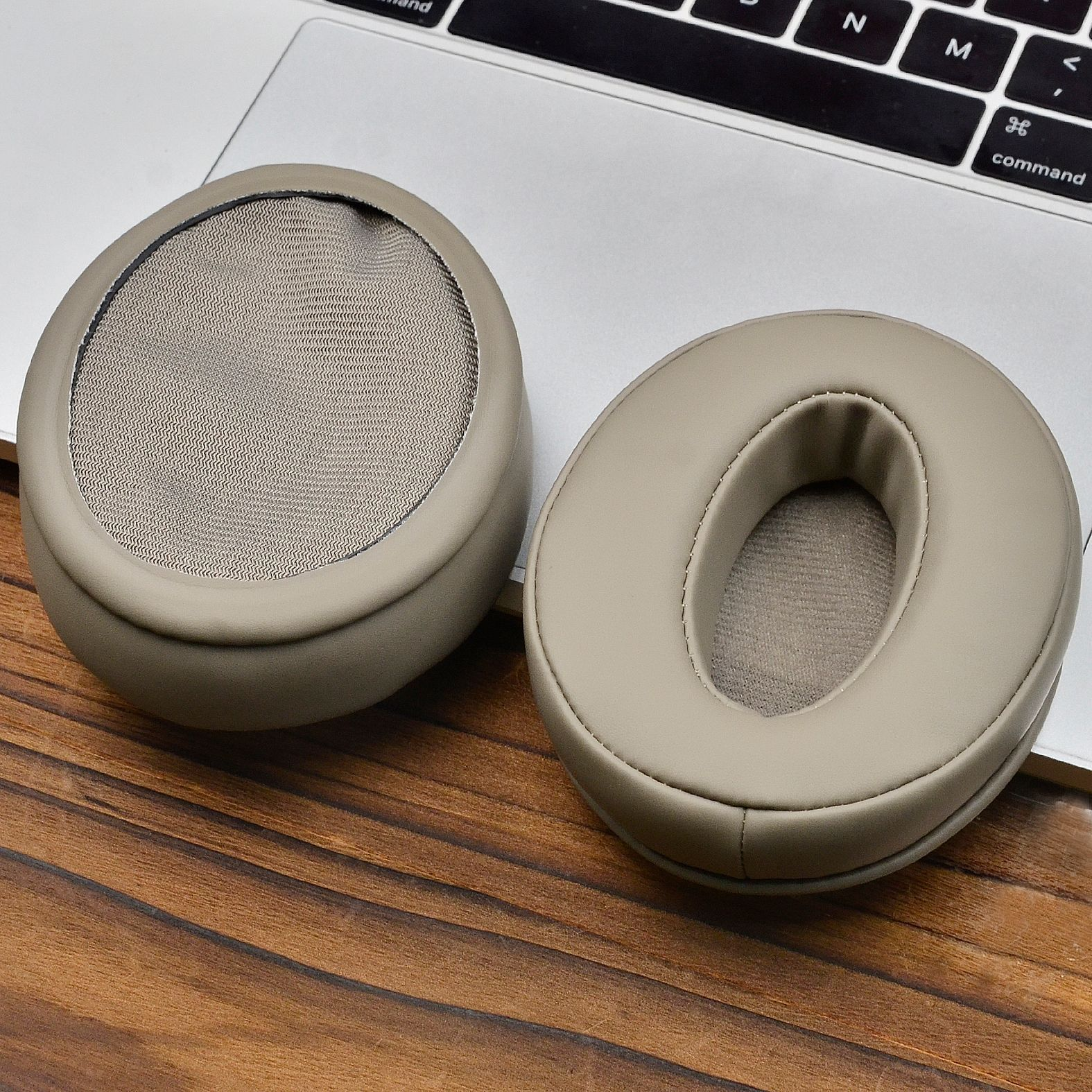 Twee beige oorkussens op een houten oppervlak en een laptop.