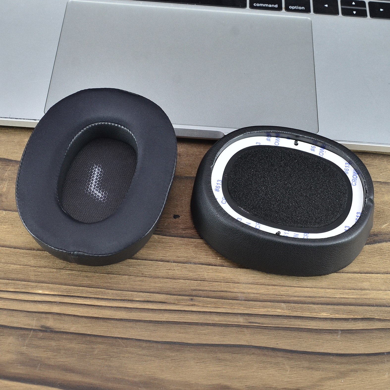 Czarne nauszniki do słuchawek, jeden z literą 'L' na wewnętrznej siatce, na drewnianej powierzchni.