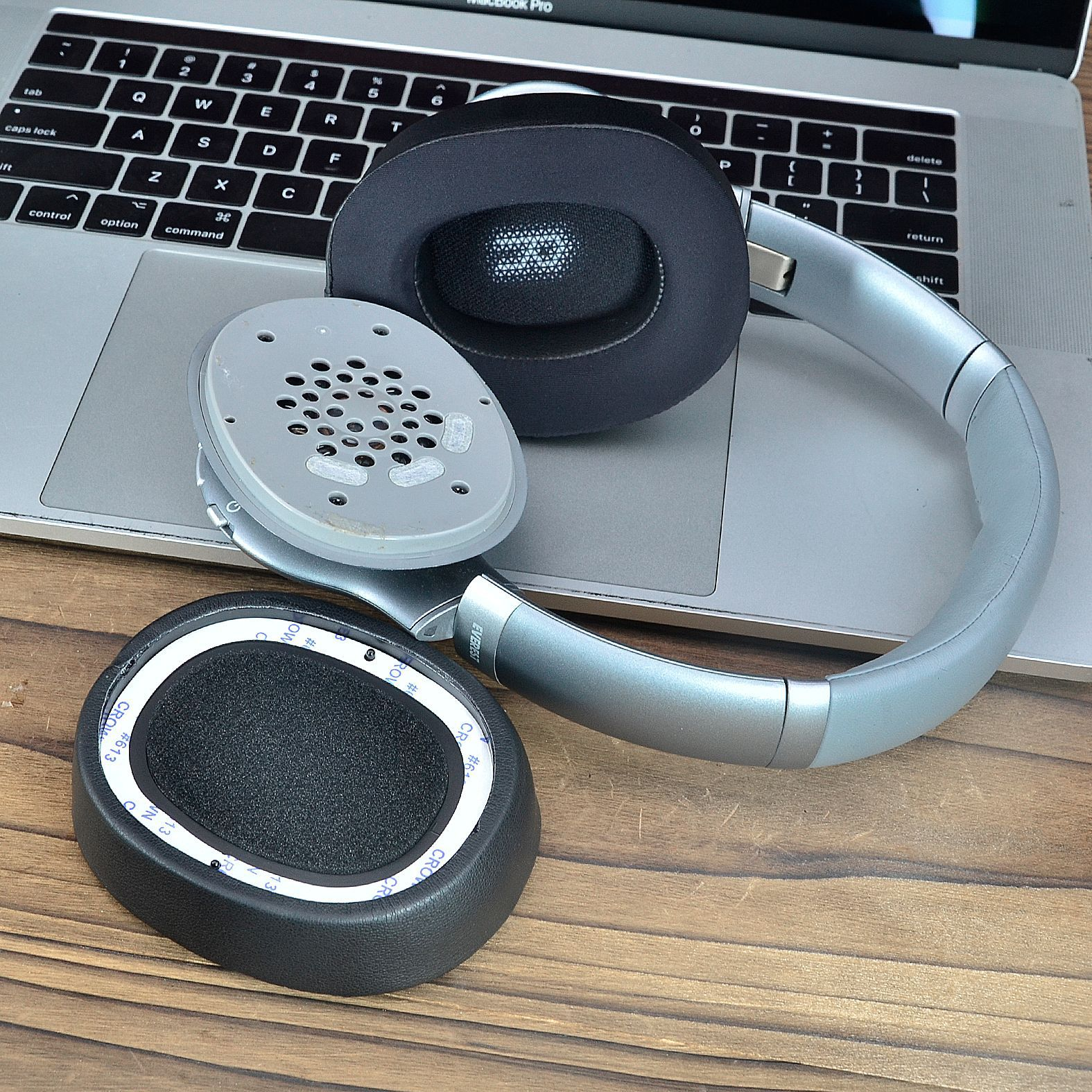 Części słuchawek obok laptopa. Obejmuje nauszniki, srebrną ramę i głośnik wewnętrzny.