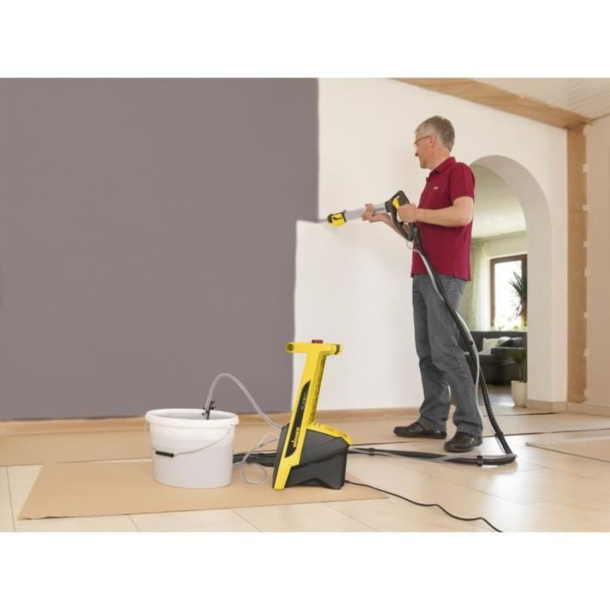 Eine Person sprüht mit einem gelb-schwarzen Farbsprühgerät Farbe auf eine Wand, in der Nähe eines weißen Eimers.