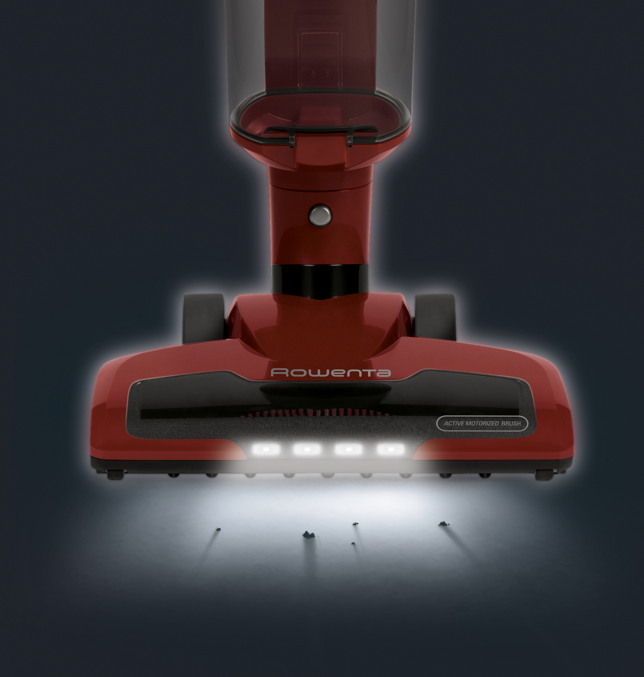 Ein roter Staubsaugerkopf mit Lichtern und Rowenta-Logo. Kleine Partikel werden am Boden beleuchtet.